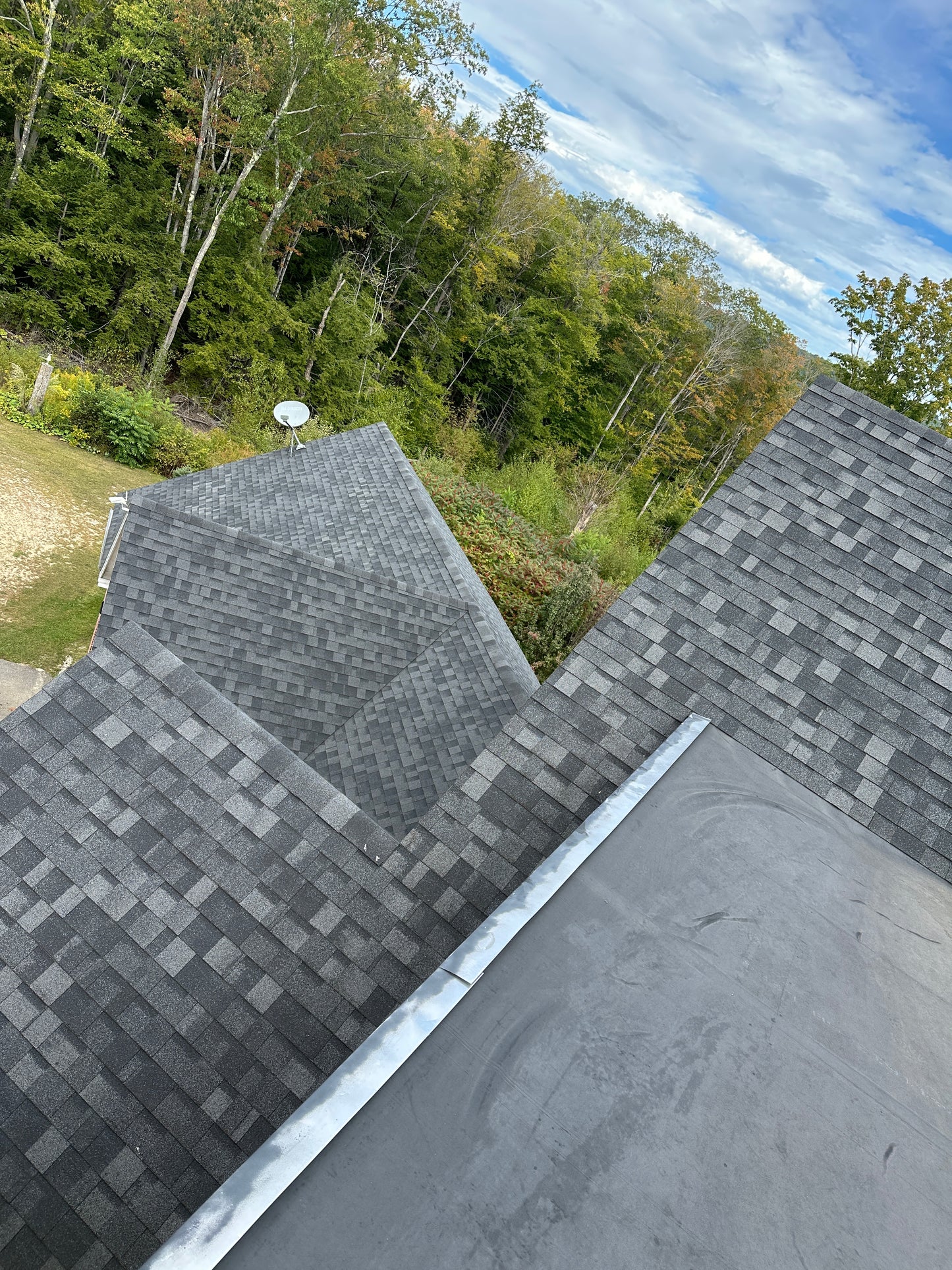 Roof with new shingles and a view of trees and sky.