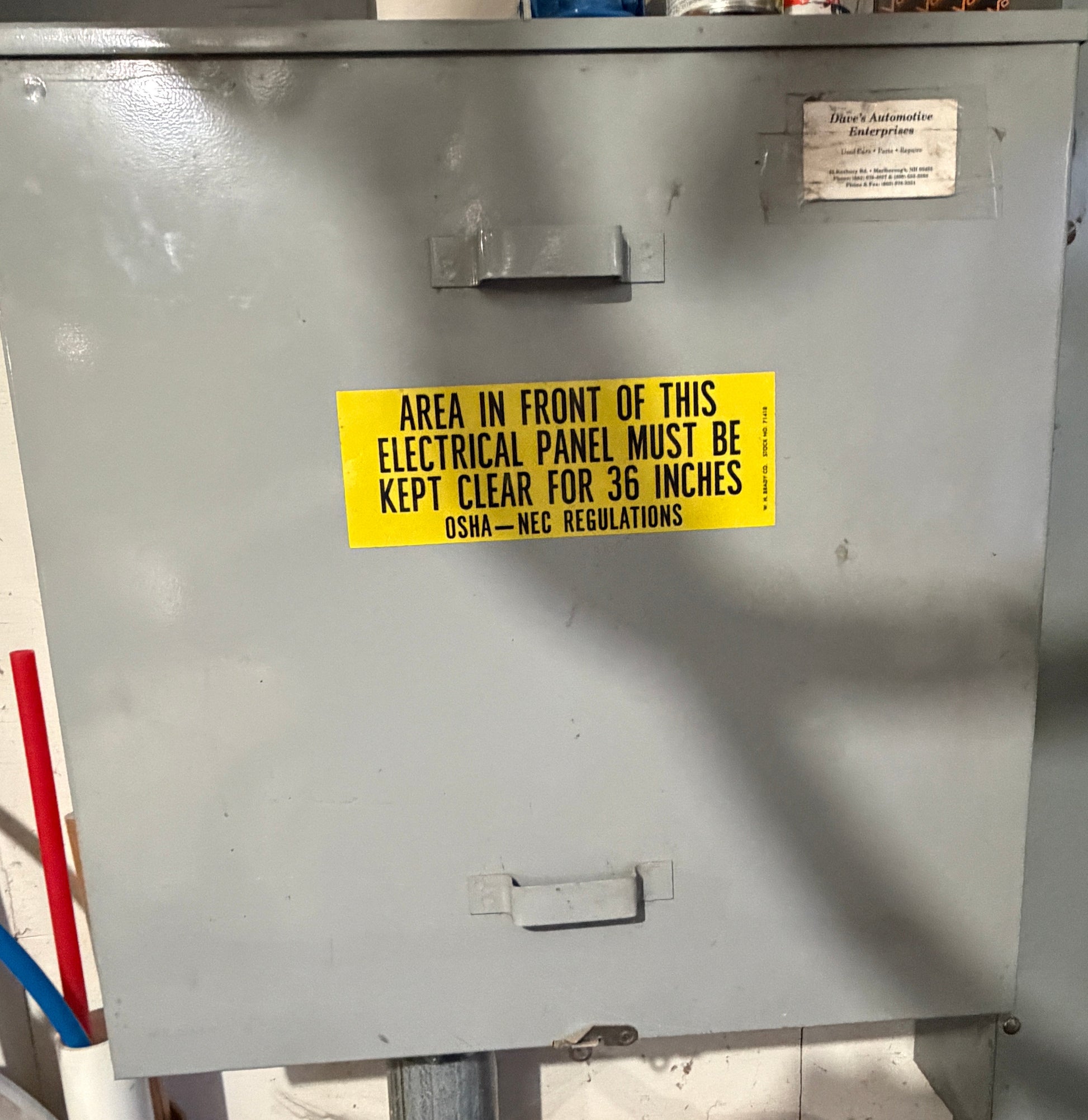 Metal electrical panel with a yellow warning label on a cluttered background
