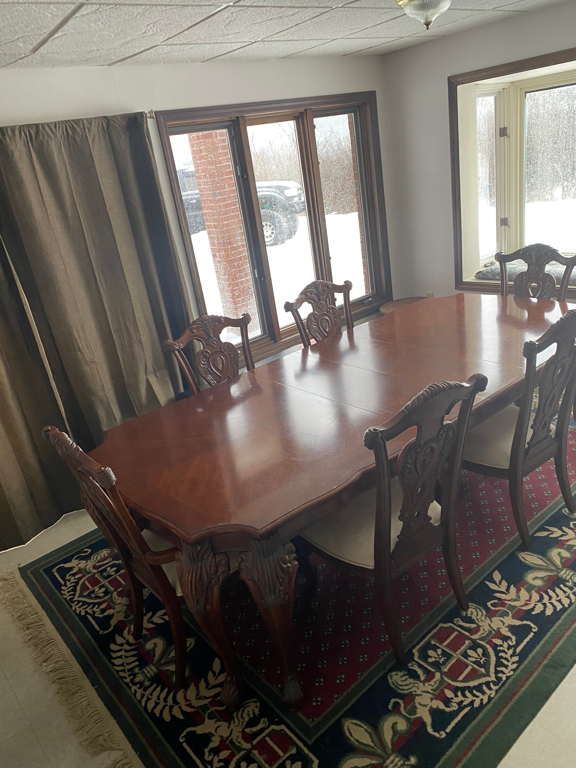 Dining room with wooden table and chairs on a patterned rug near a window.