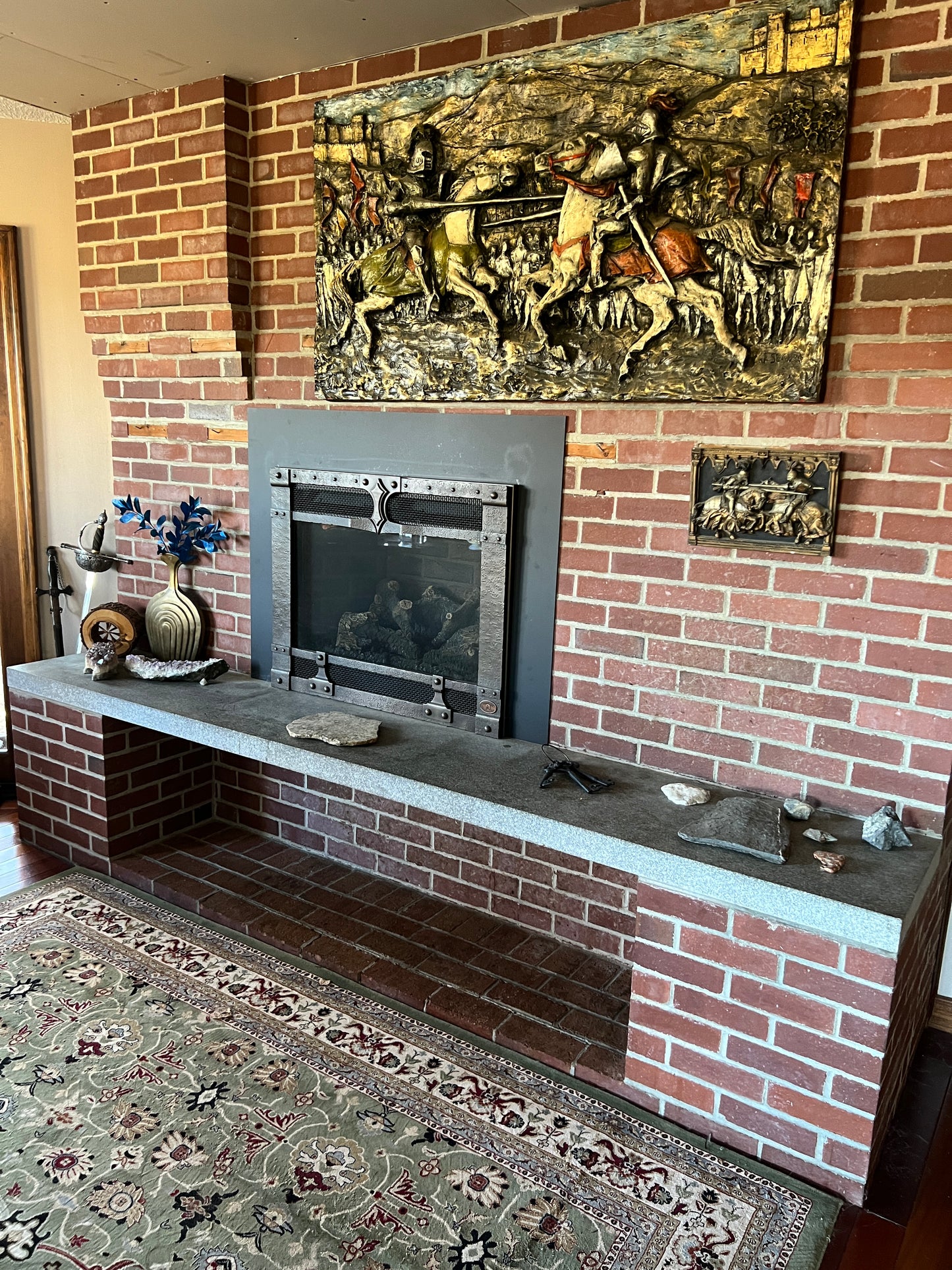 Decorative fireplace with artwork on the wall and a patterned rug.