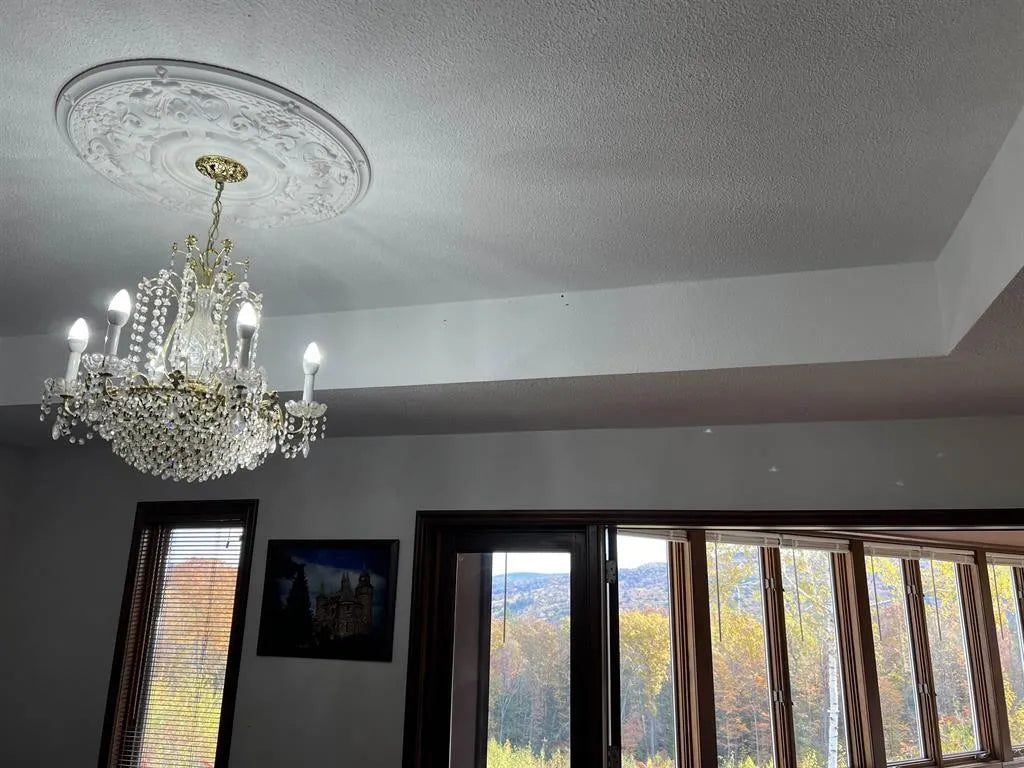Chandelier hanging from a ceiling with windows showing a scenic view outside.