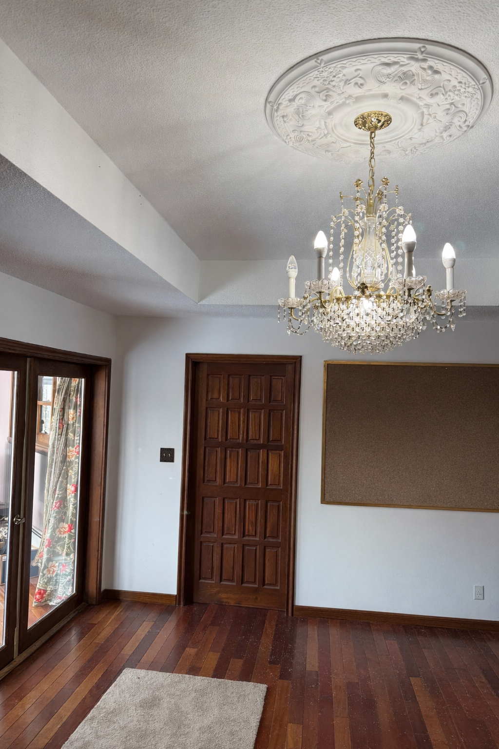 Chandelier hanging in a room with wooden floors and a large window.
