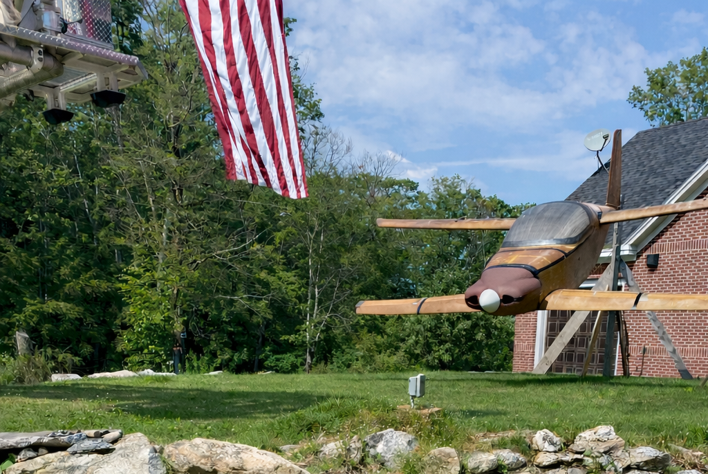 A small airplane model on a stone wall with a house and American flag in the background.