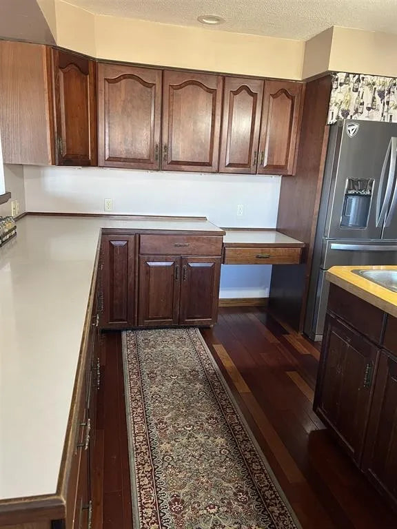 Kitchen with wooden cabinets, a refrigerator, and a patterned rug on the floor.