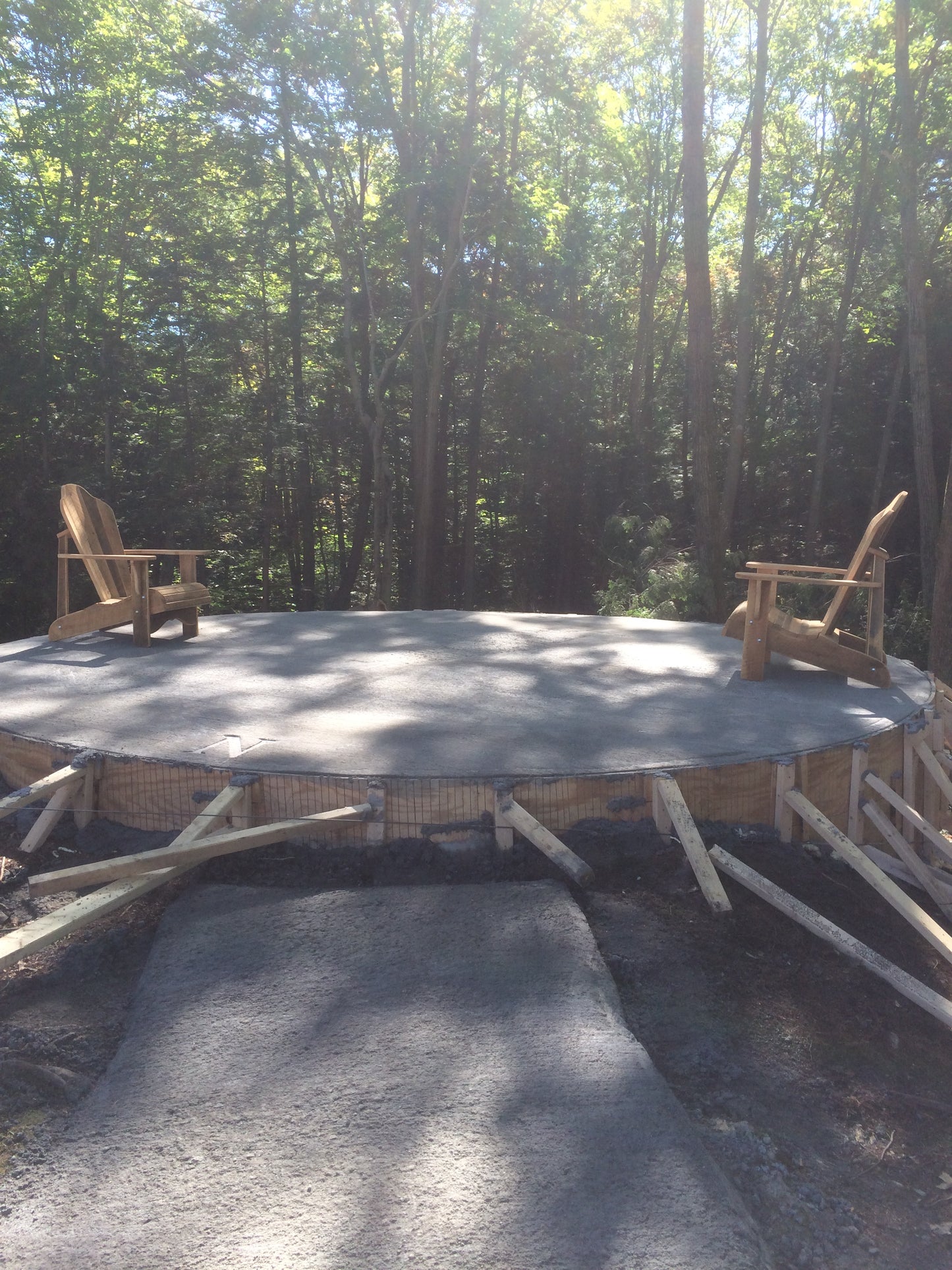 The first chairs on the platform. wood supports around fire pit in a forest setting with two Adirondack chairs.