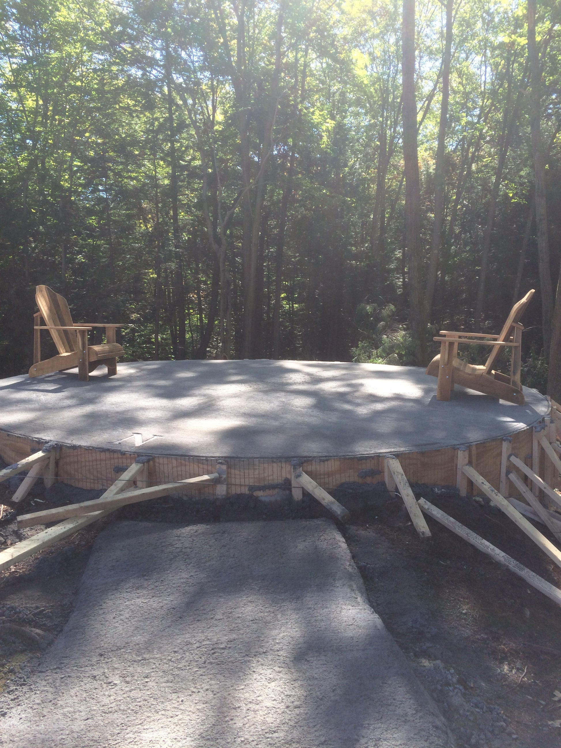 The first chairs on the platform. wood supports around fire pit in a forest setting with two Adirondack chairs.