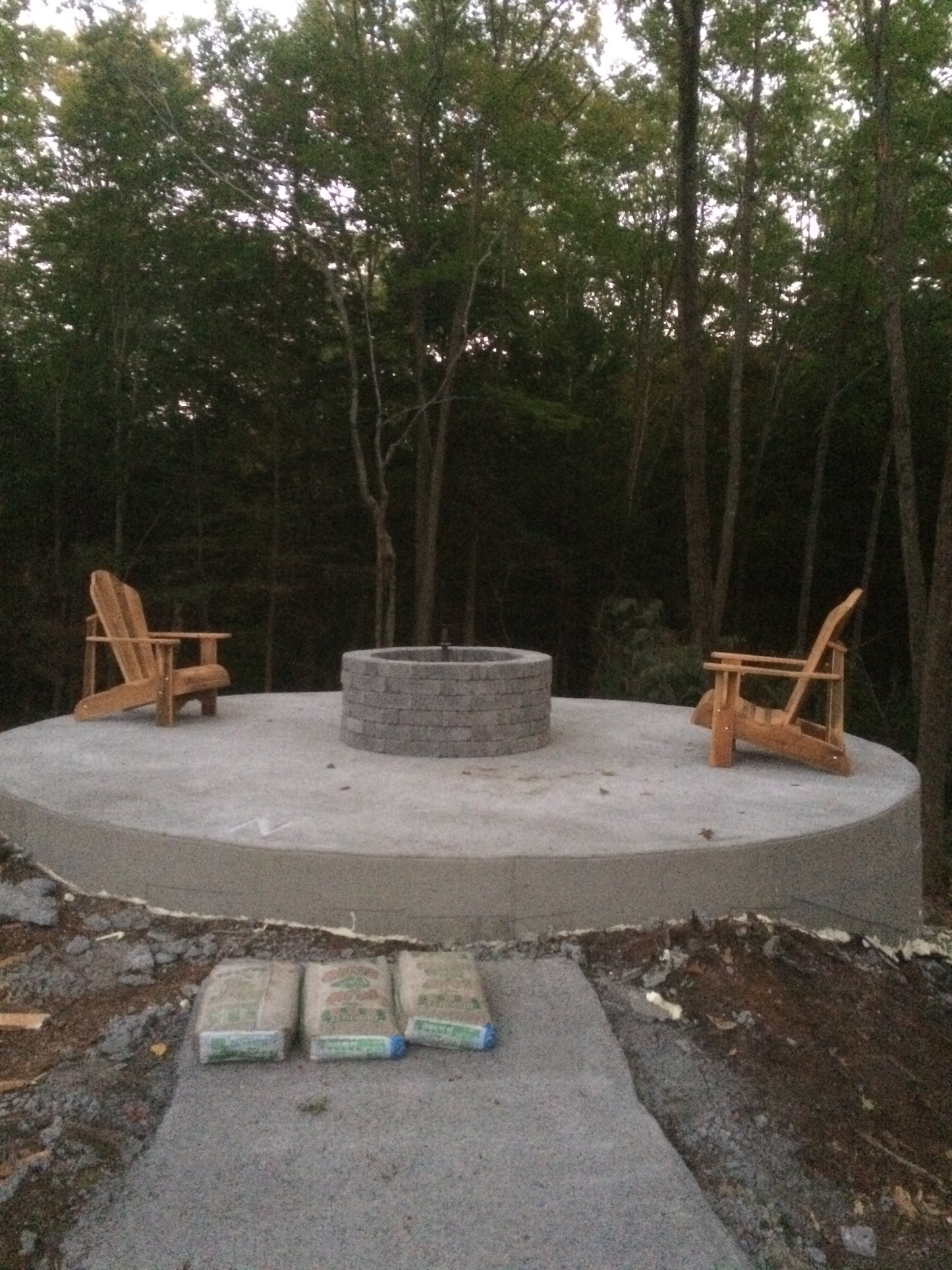 Concrete patio with wooden chairs and a fire pit in a forest setting