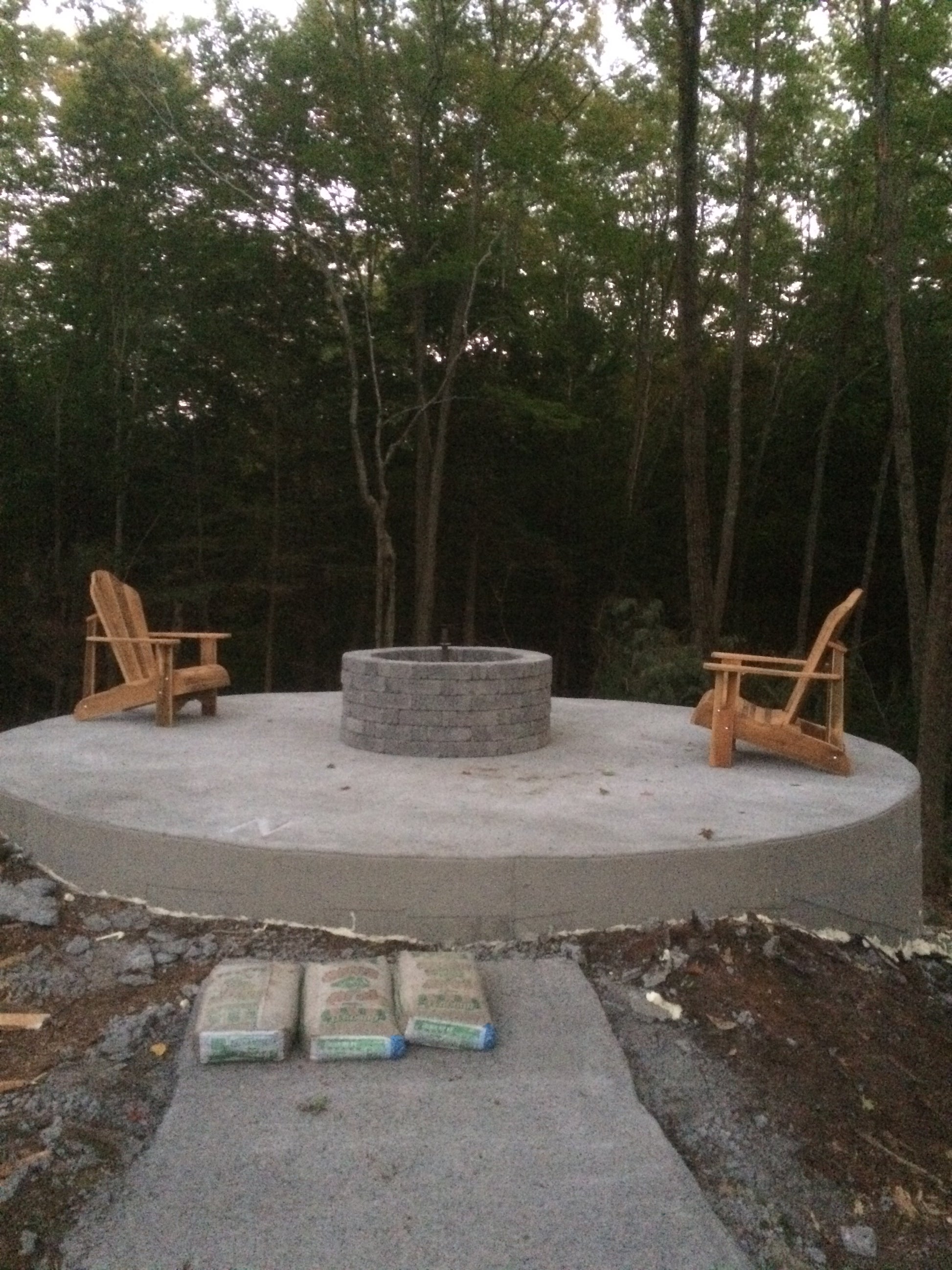 Concrete patio with wooden chairs and a fire pit in a forest setting