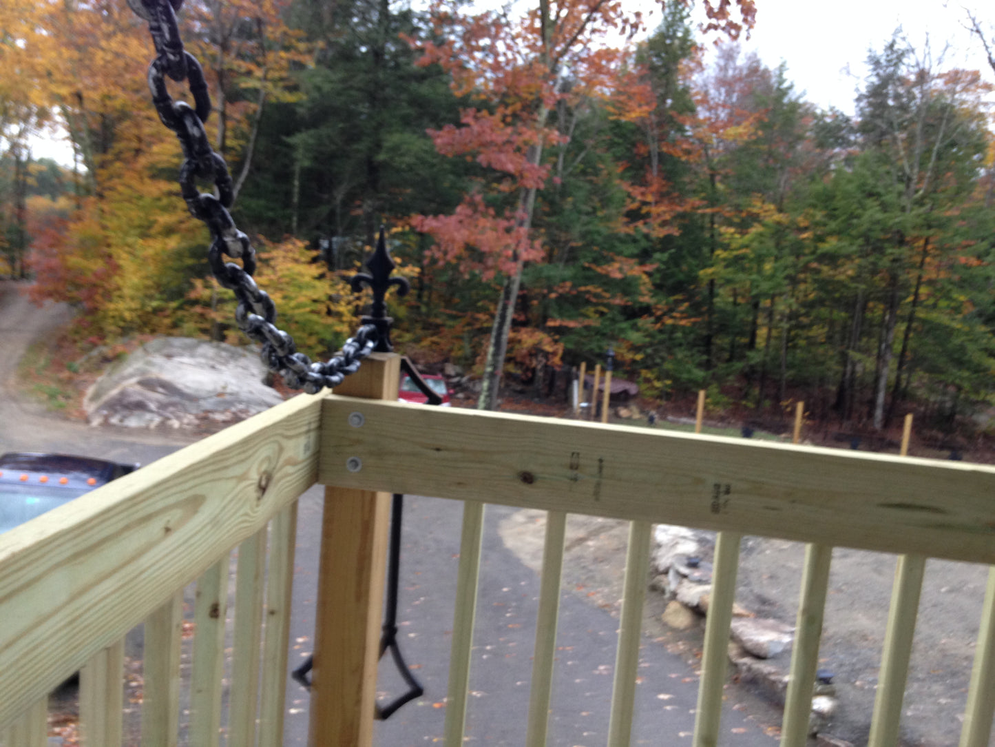 Wooden deck  draw bridge style railing with a chain, overlooking a forest with autumn foliage.