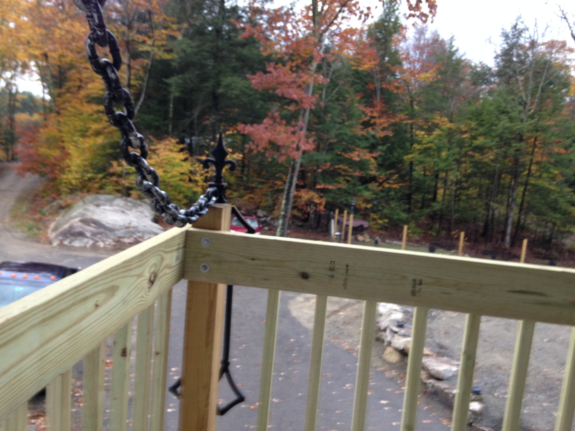 Wooden deck  draw bridge style railing with a chain, overlooking a forest with autumn foliage.