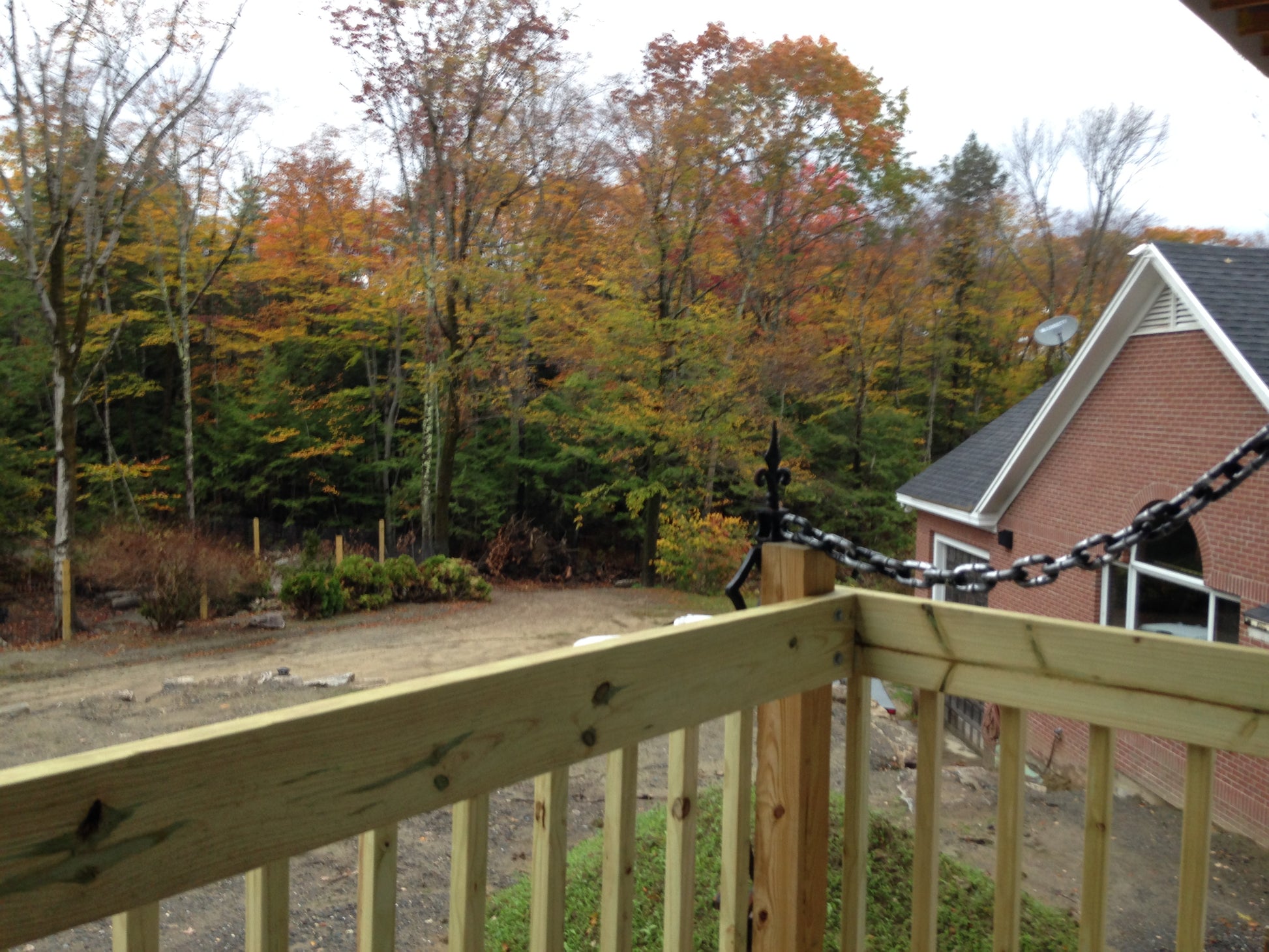 View from a deck with a wooden railing overlooking a house and autumn trees.