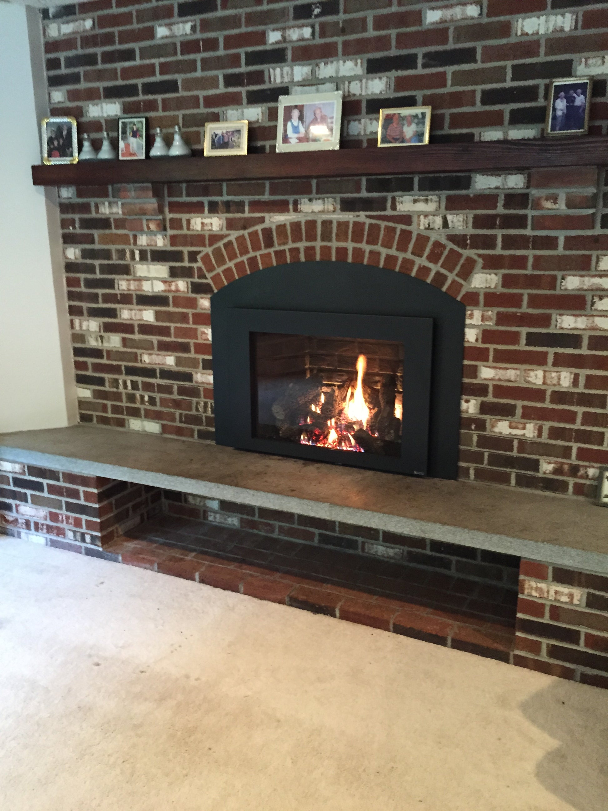 Fireplace with a lit fire inside, surrounded by decorative tiles on a brick wall.