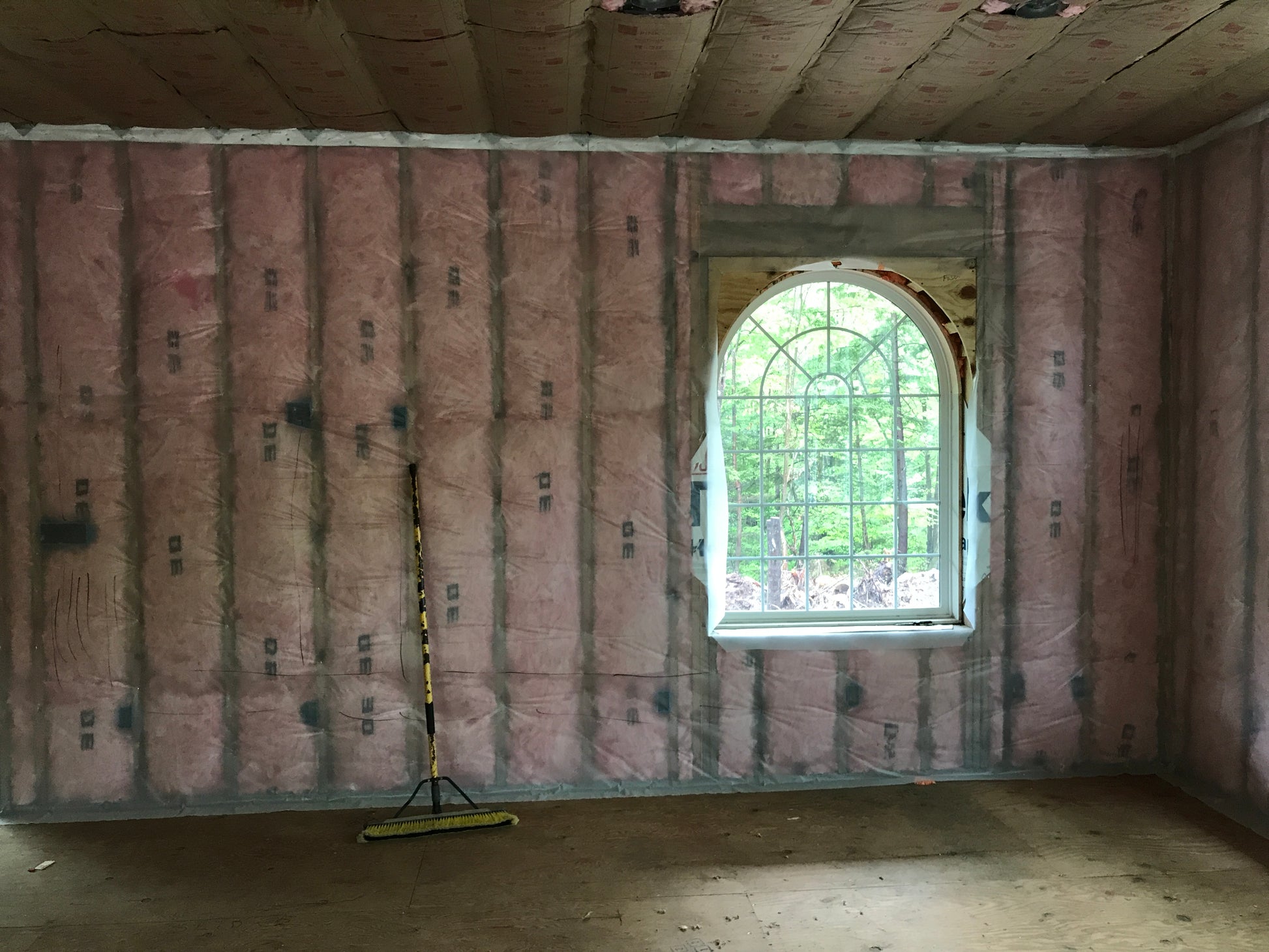 Room under construction with pink insulation on the walls and a large window.