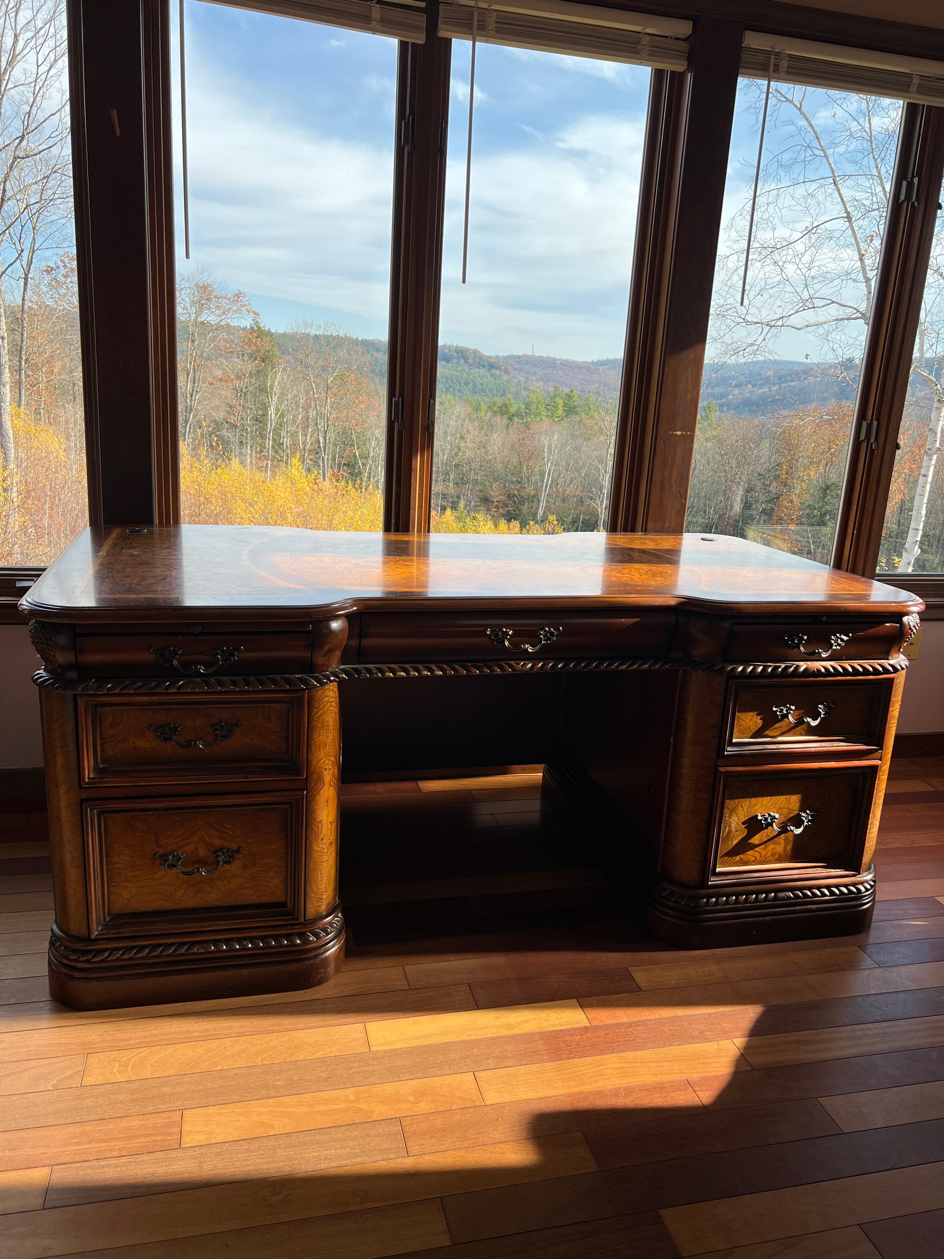 Office area  is a great place to work wooden desk with drawers in a room with large windows showing a view of trees and sky.
