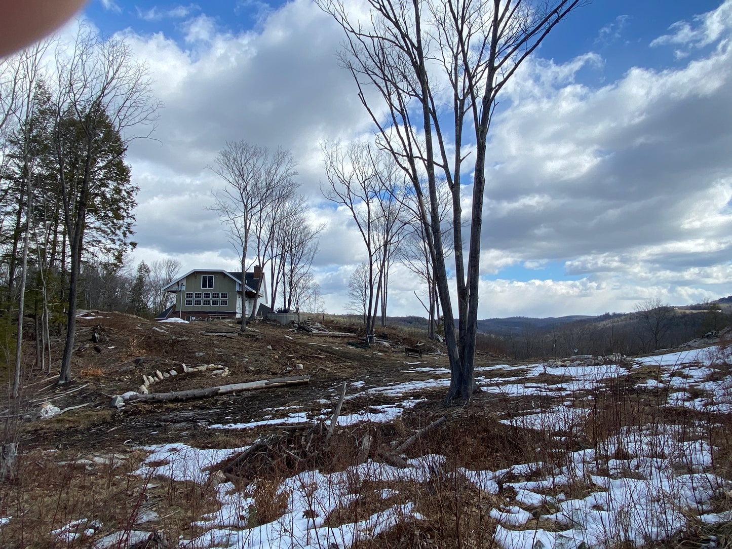 Houses on a  mountain top with trees and snow under a cloudy sky. Cleaning up and getting ready to plant lawns.