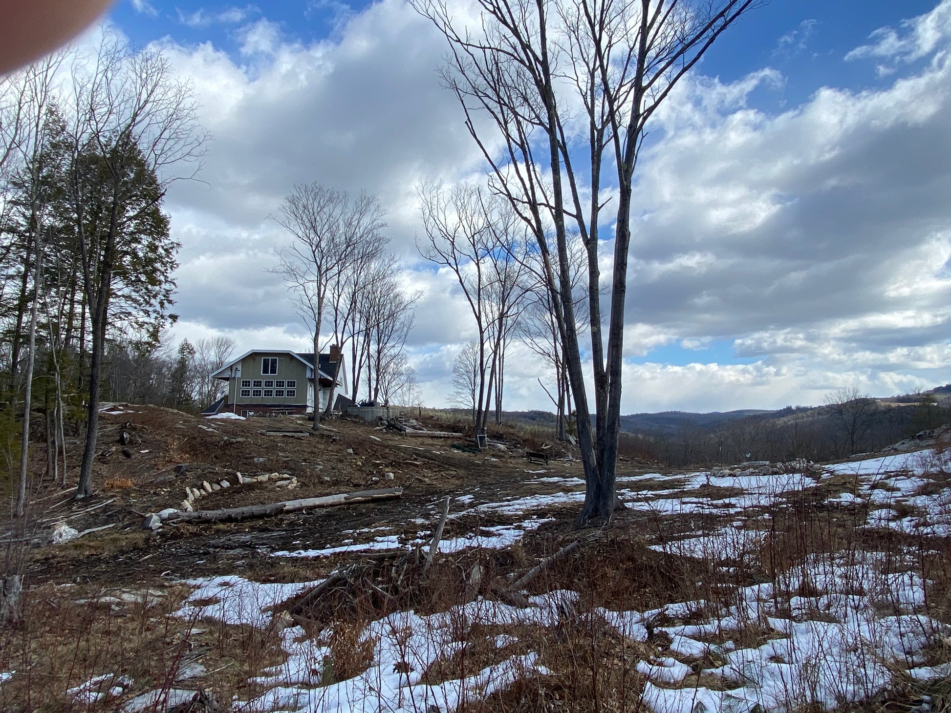 Houses on a  mountain top with trees and snow under a cloudy sky. Cleaning up and getting ready to plant lawns.