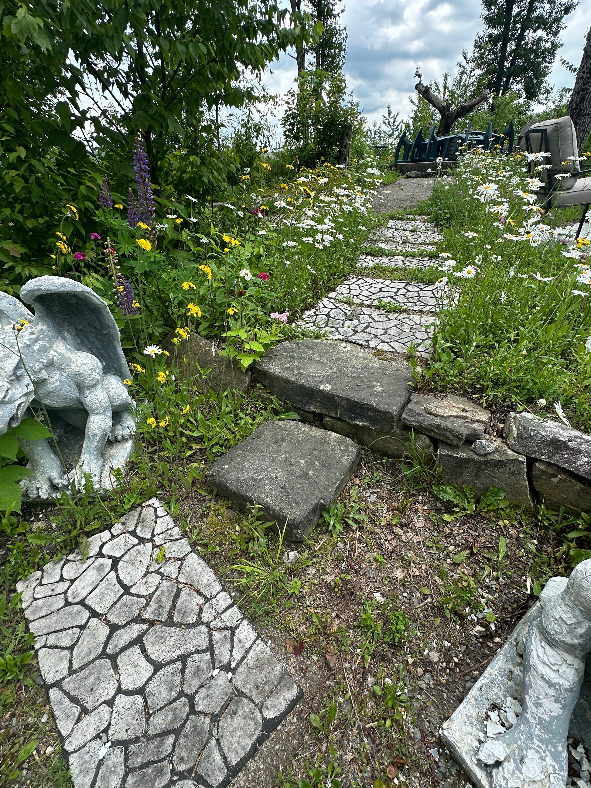 Garden with stone pathway, statues, and flowers on a cloudy day