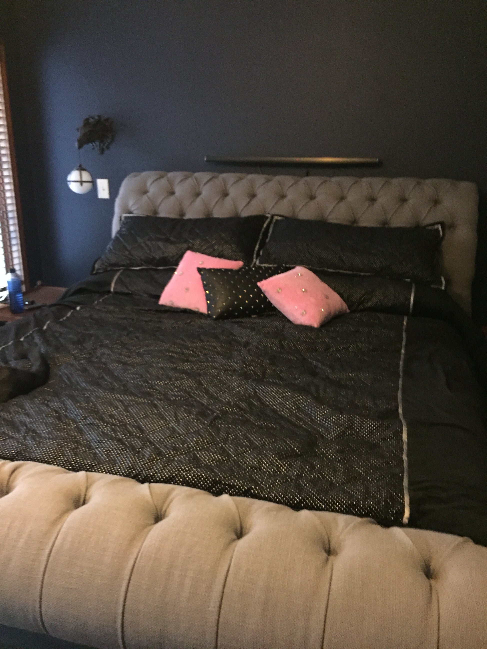 Black  bed outfit with pink accents standing between two beige cushioned  headboard on walls.