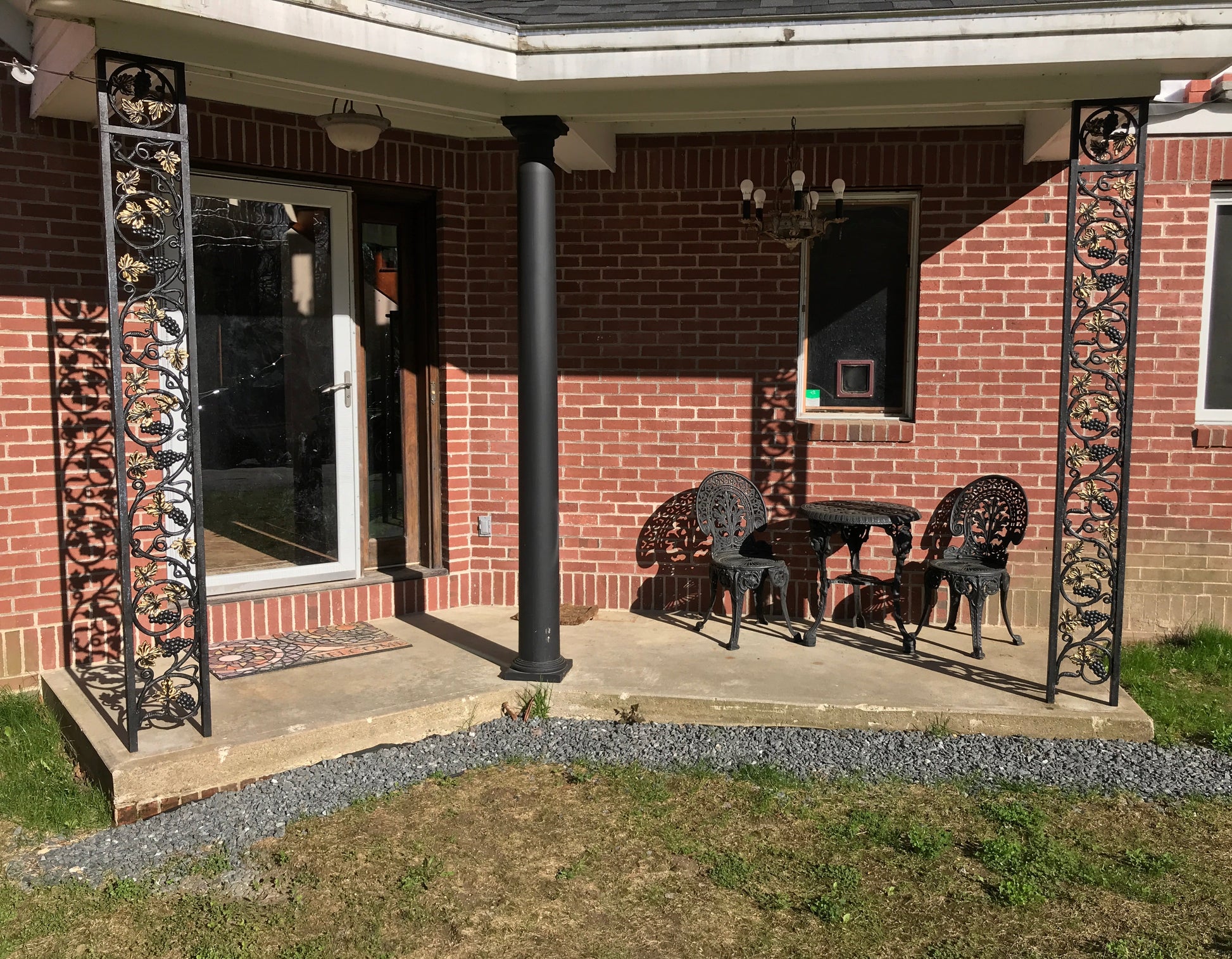 Patio with wrought iron posts and outdoor wrought iron furniture under a brick building with chandelier.