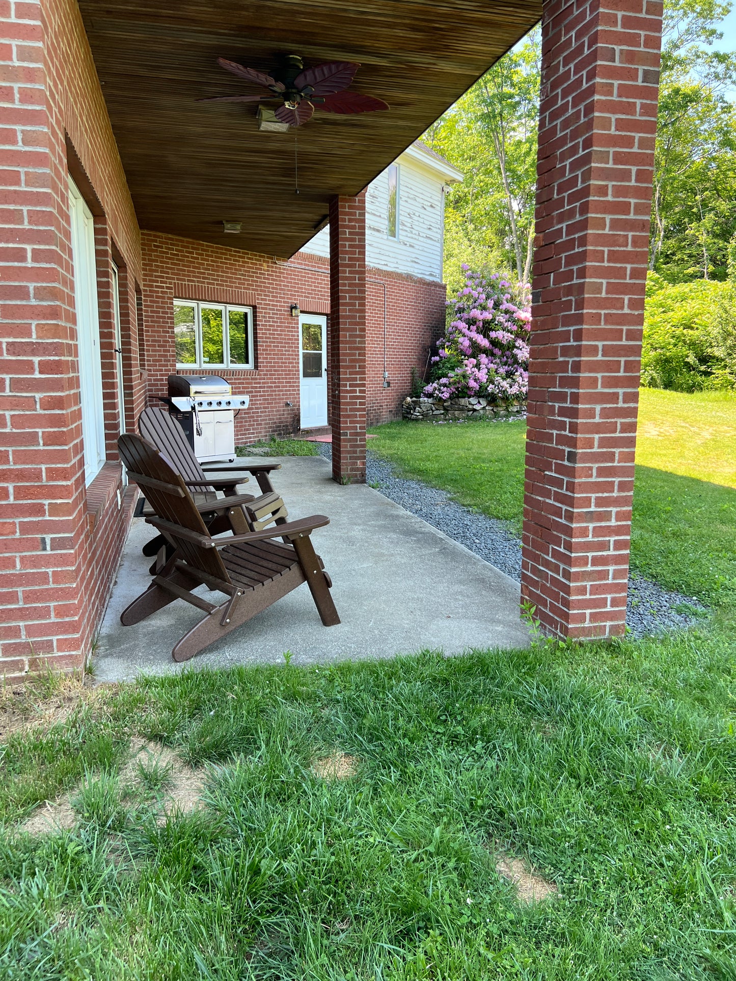 Outdoor  Patio seating area with wooden  Adirondack chairs on a patio, leading to a brick building.