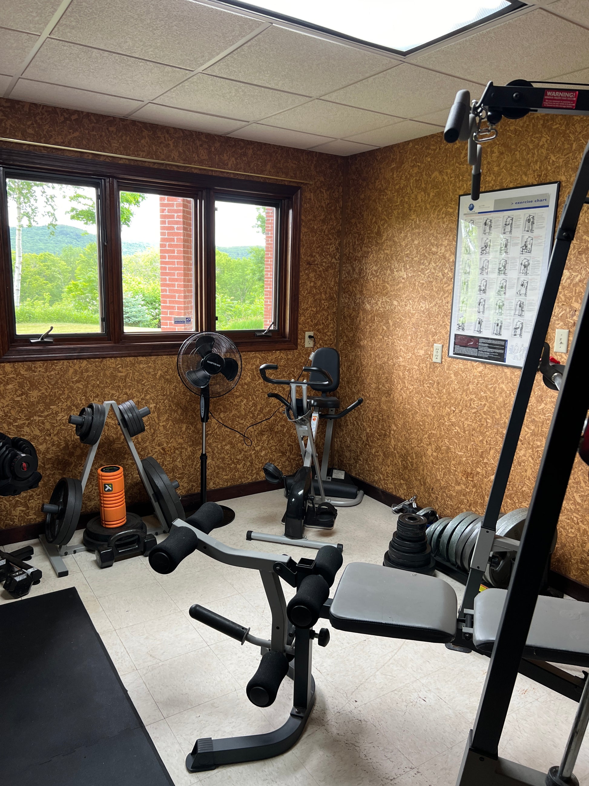 Home gym setup with weightlifting equipment in a room with a window and tiled floor.