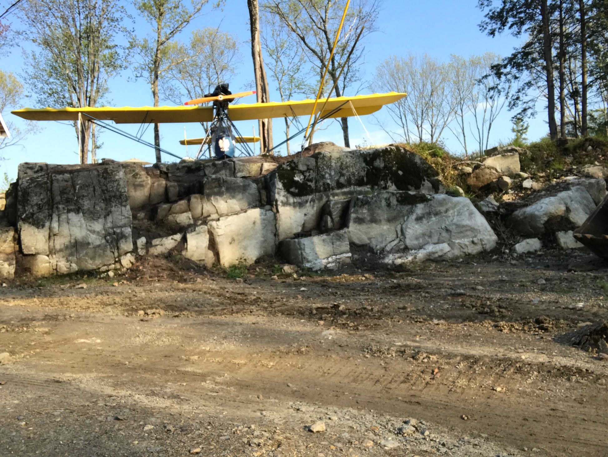 Yellow biplane on a rocky outcrop with trees in the background