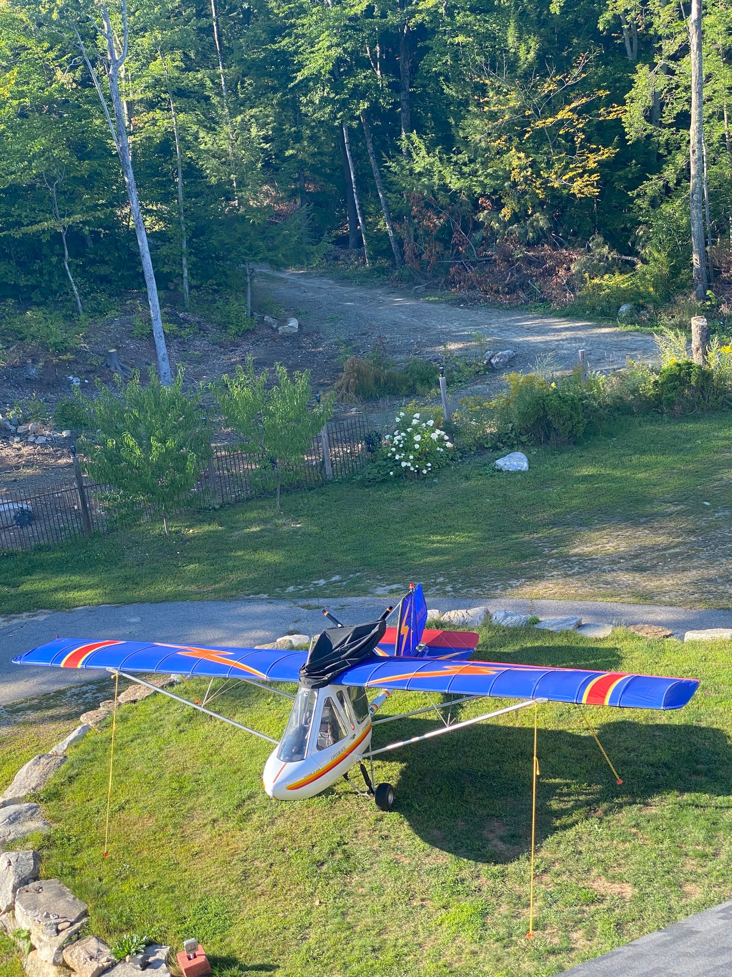 Small airplane with a colorful tail flying over a road and greenery