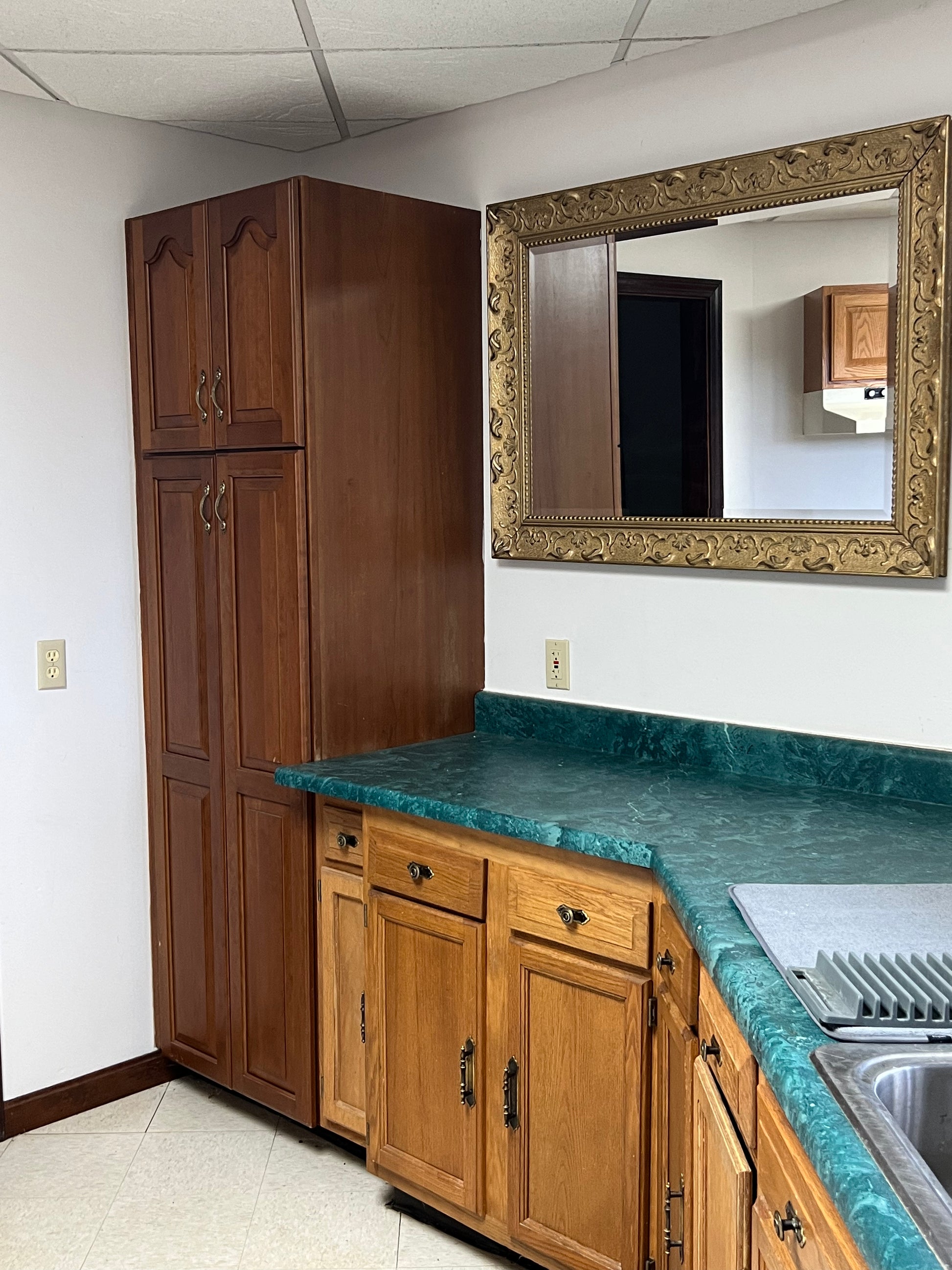 Kitchen with wooden cabinets, teal countertop, and decorative mirror.