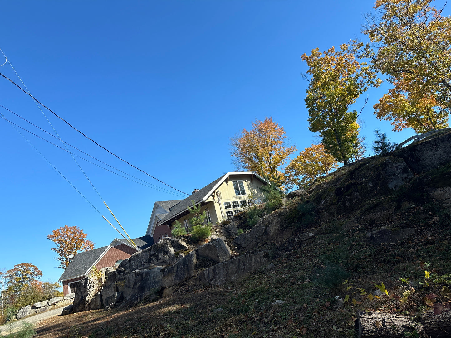 Mansion with huge rocky ledges in front with trees and clear blue sky