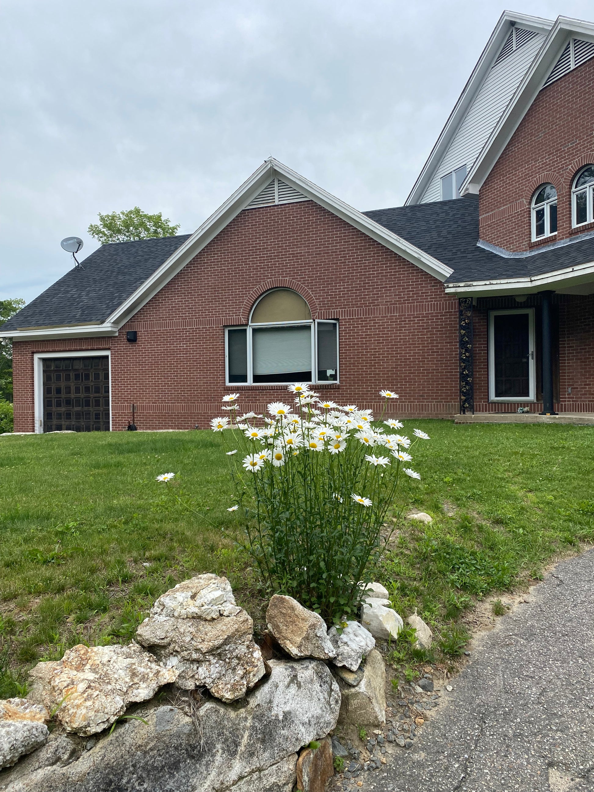 Brick house with  wildflowers and a grassy area and stone wall