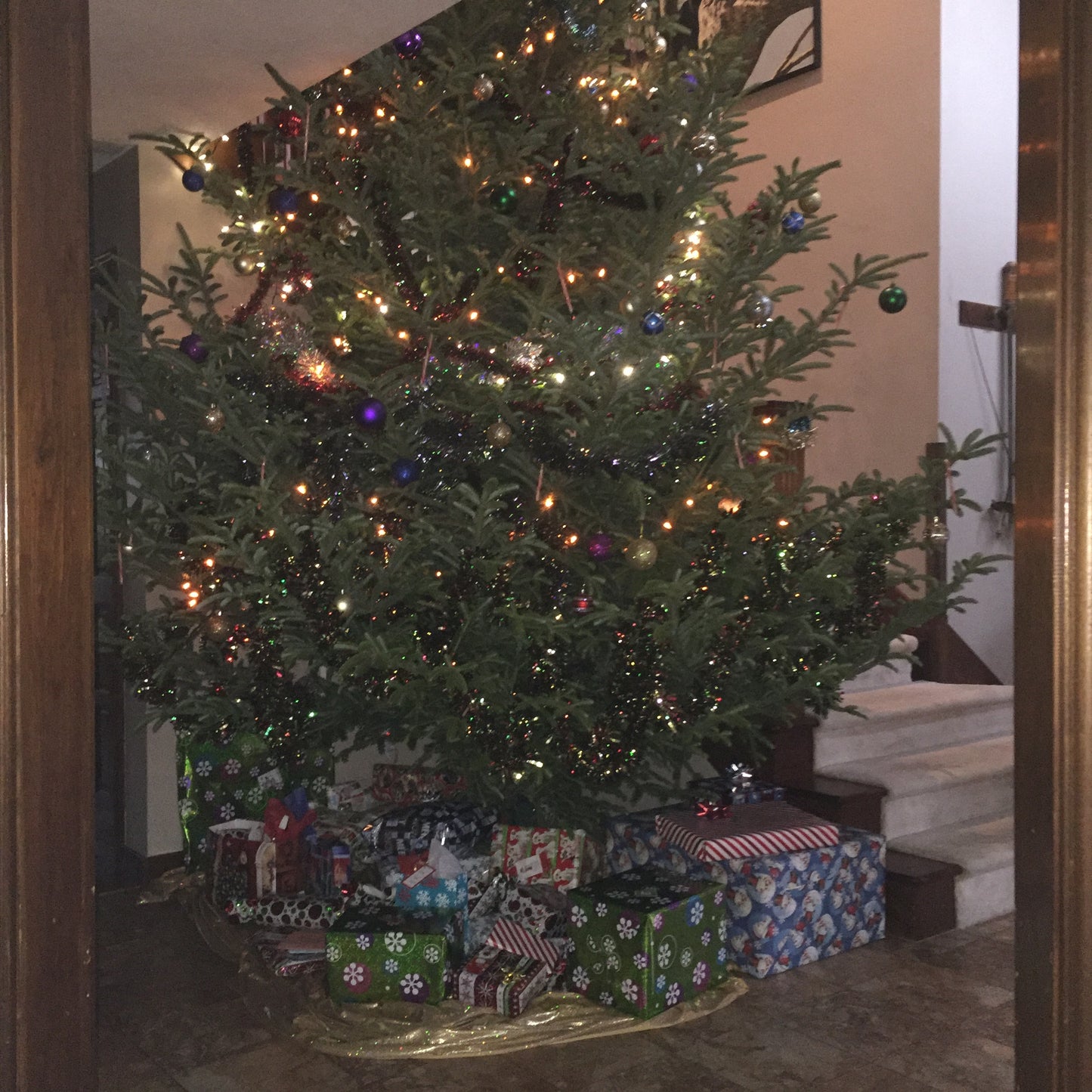 Decorated Christmas tree with lights and ornaments in a room with presents underneath.
