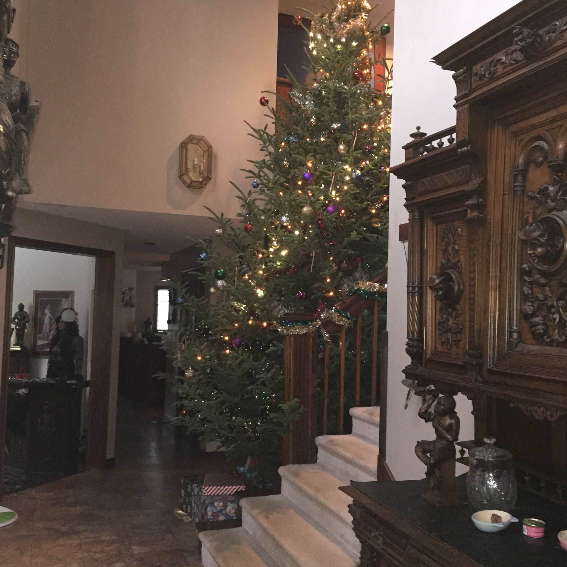 Decorated Christmas tree with lights in a room with ornate wooden furniture.
