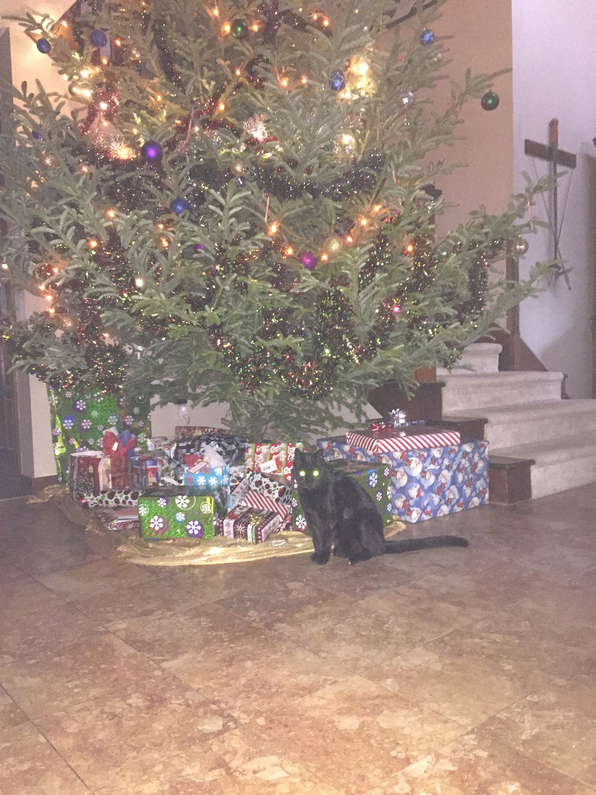 Decorated Christmas tree with presents underneath on a wooden floor.