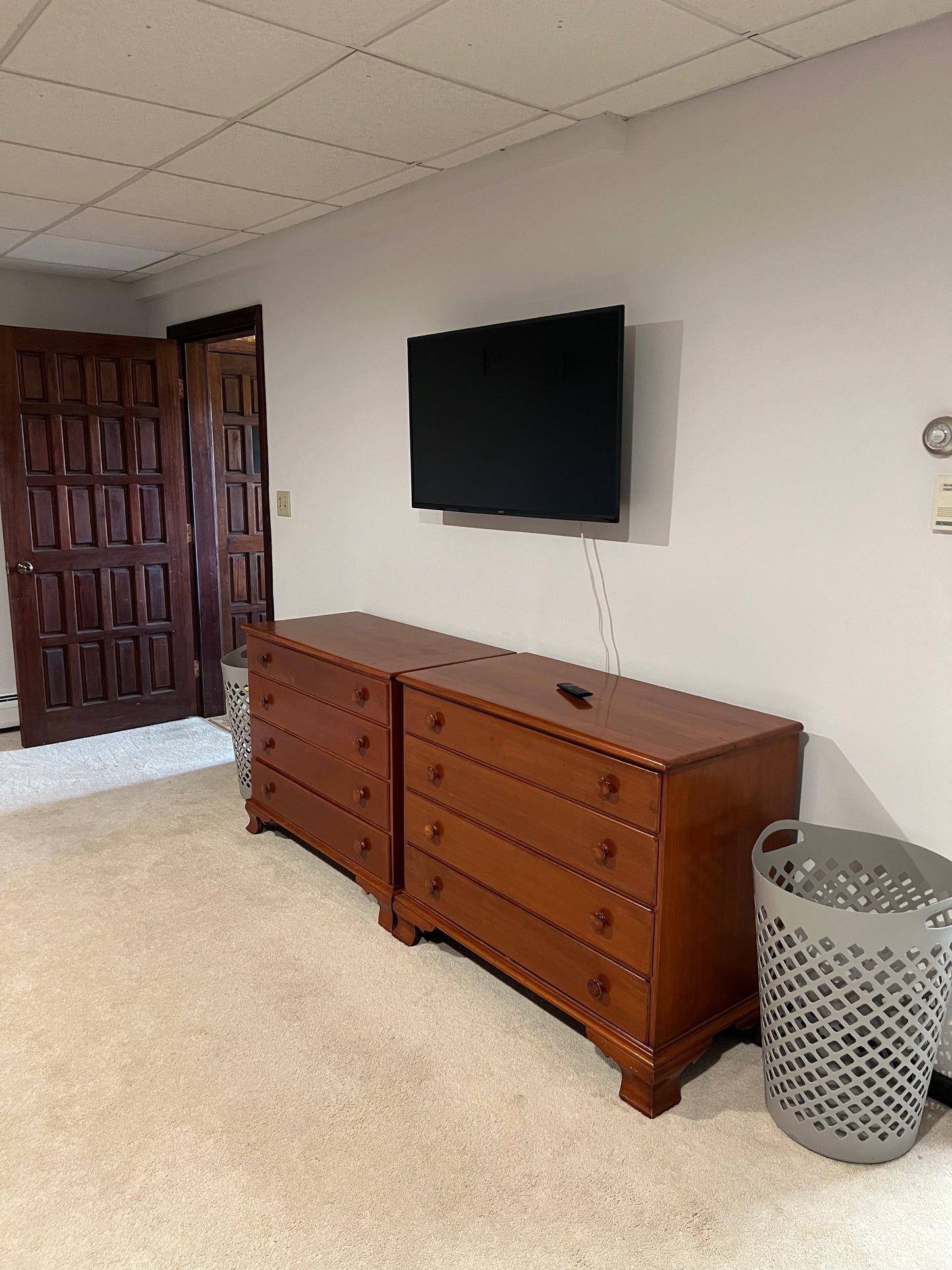 Wooden dresser with a television mounted on the wall in a room with carpeted floor and wooden doors.