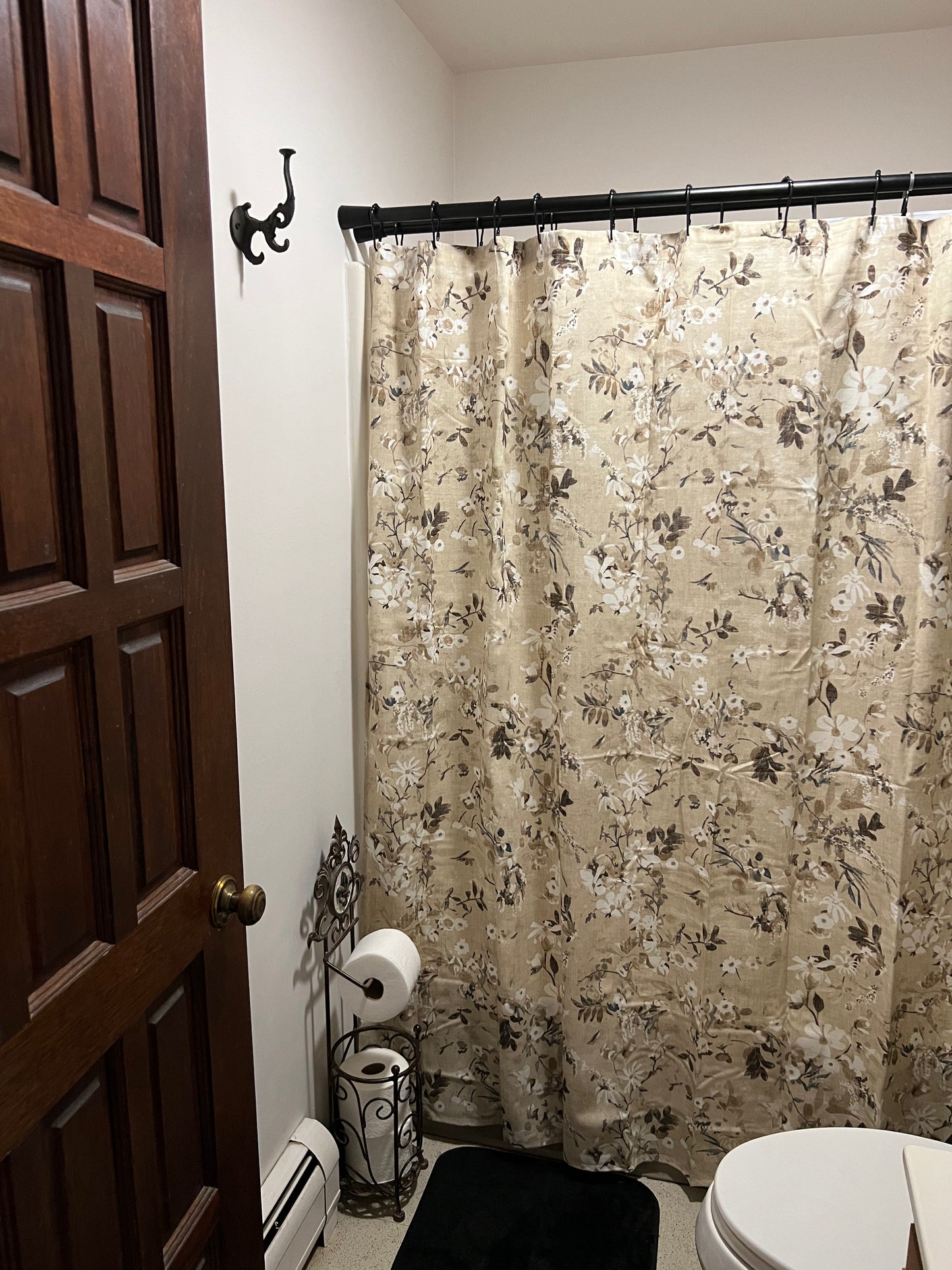 Bathroom with floral shower curtain, toilet, and toilet paper holder.