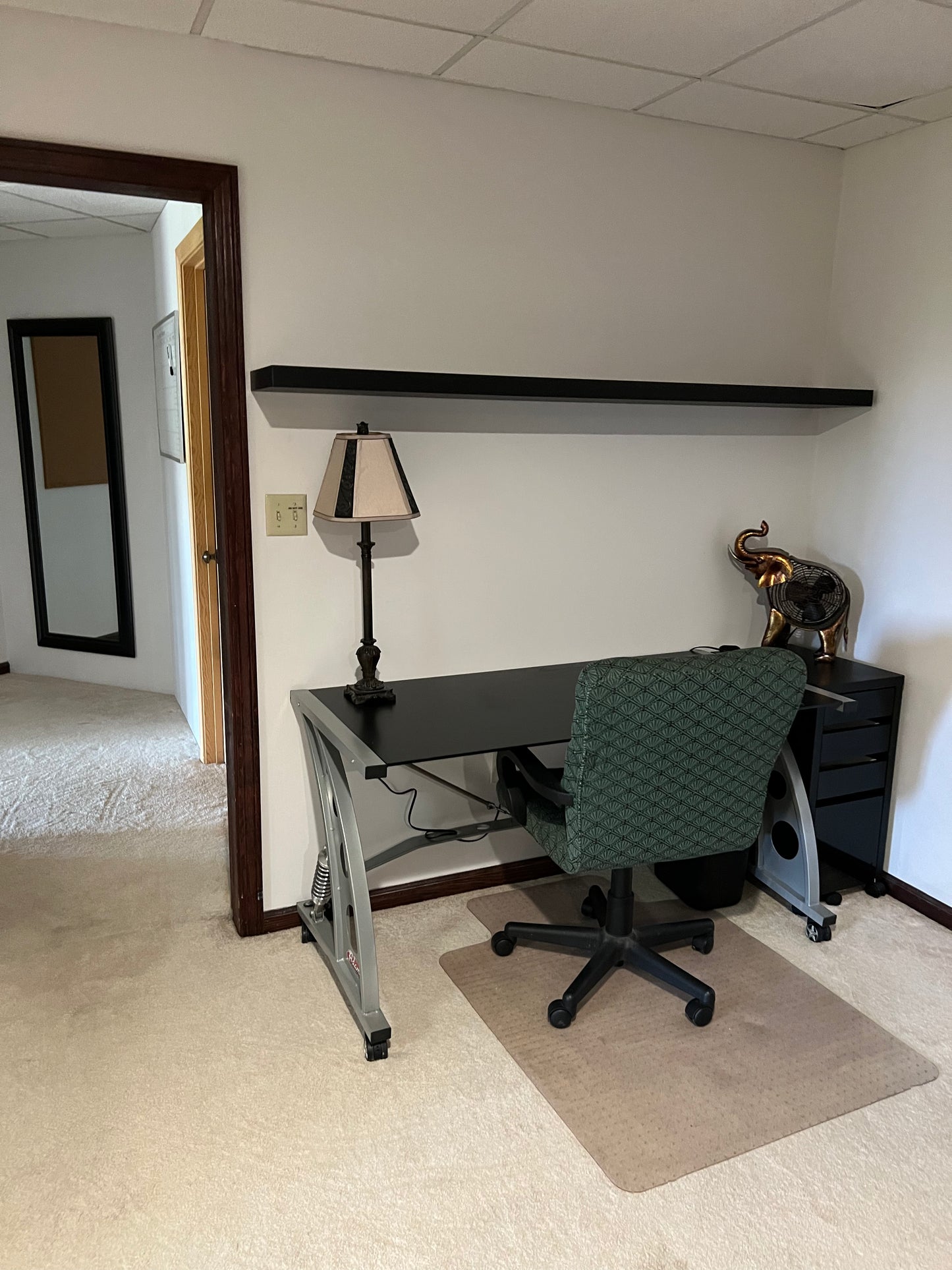 Home office with a desk, chair, and lamp in a room with carpeted floor.