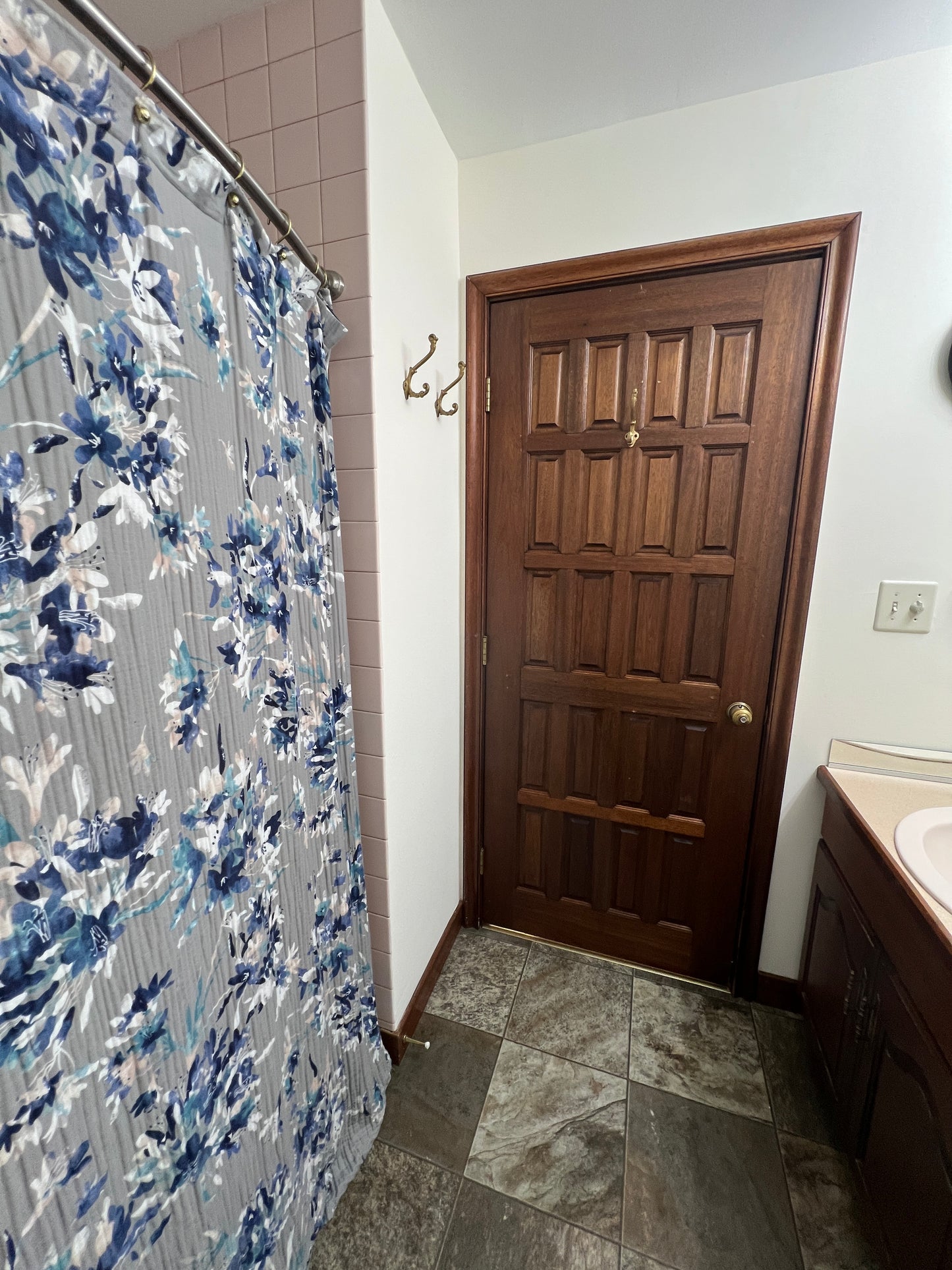 Bed with a floral bedspread in a room with a wooden door and tiled floor.