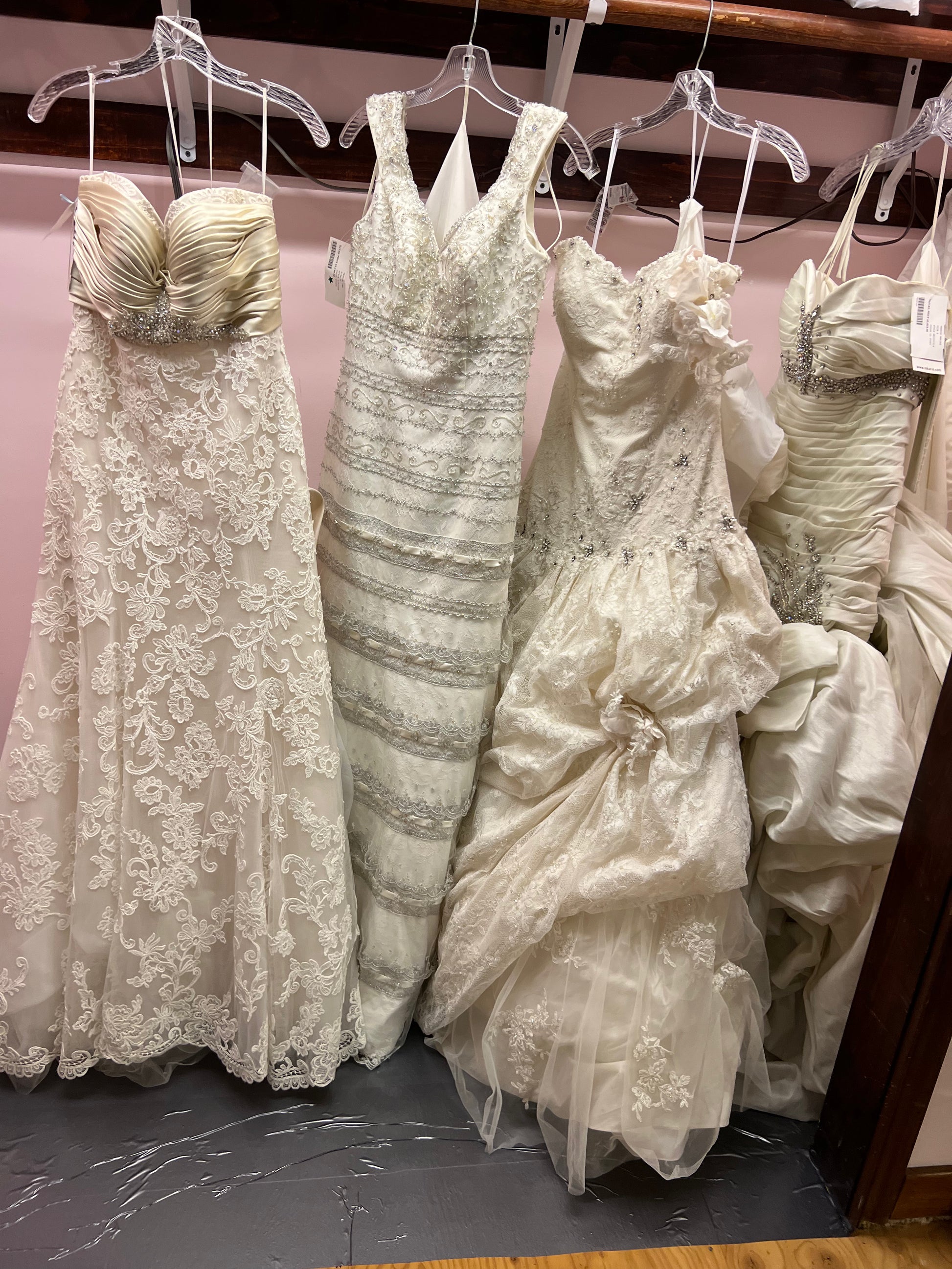 Collection of wedding dresses on hangers against a pink wall.