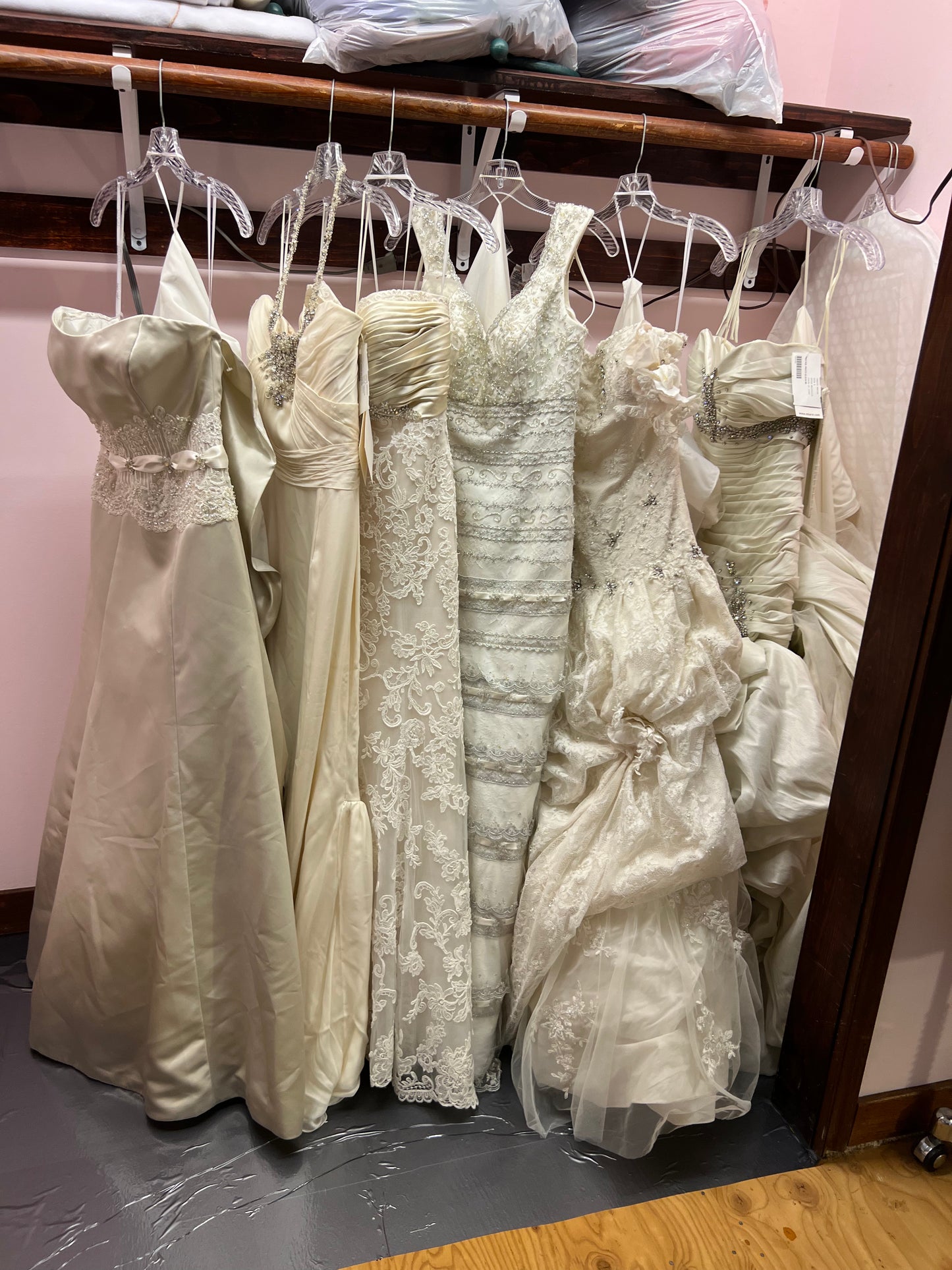Collection of wedding dresses hanging on a rack against a pink wall.