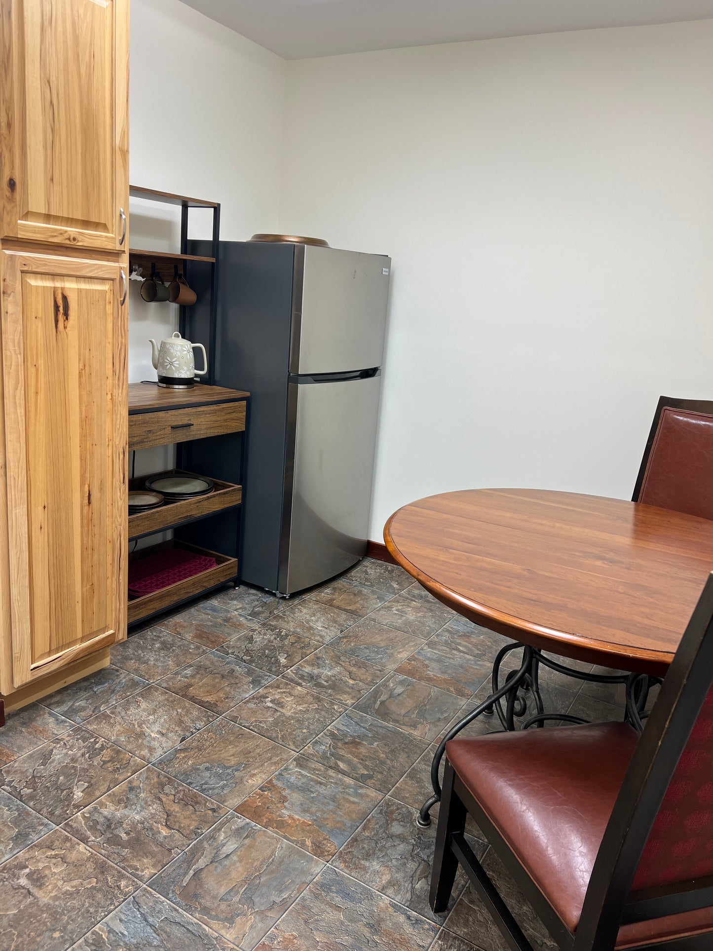 Small kitchenette with wooden cabinets, a refrigerator, and a tiled floor.