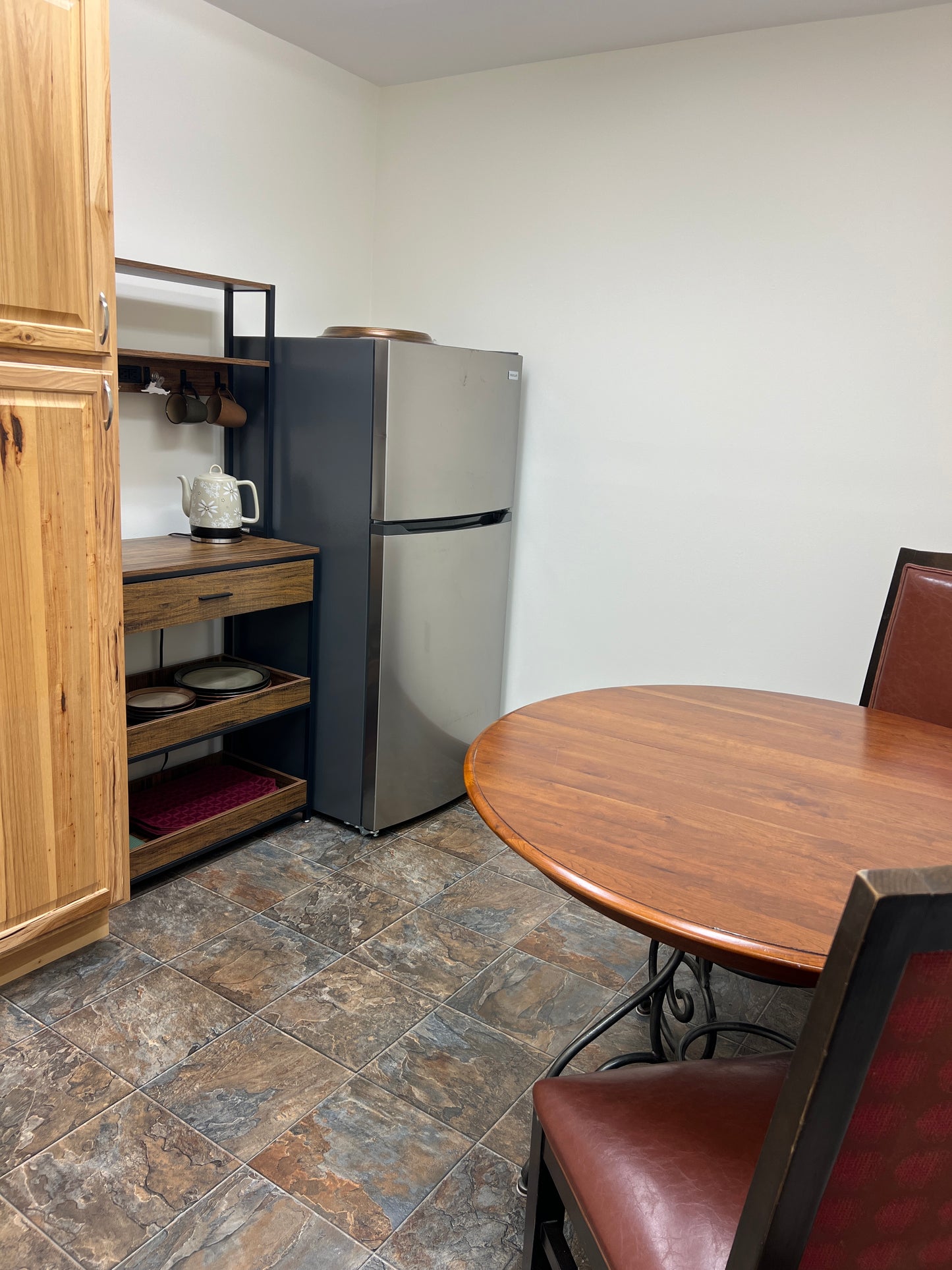 Small refrigerator in a kitchen setting with wooden cabinets and a tiled floor.