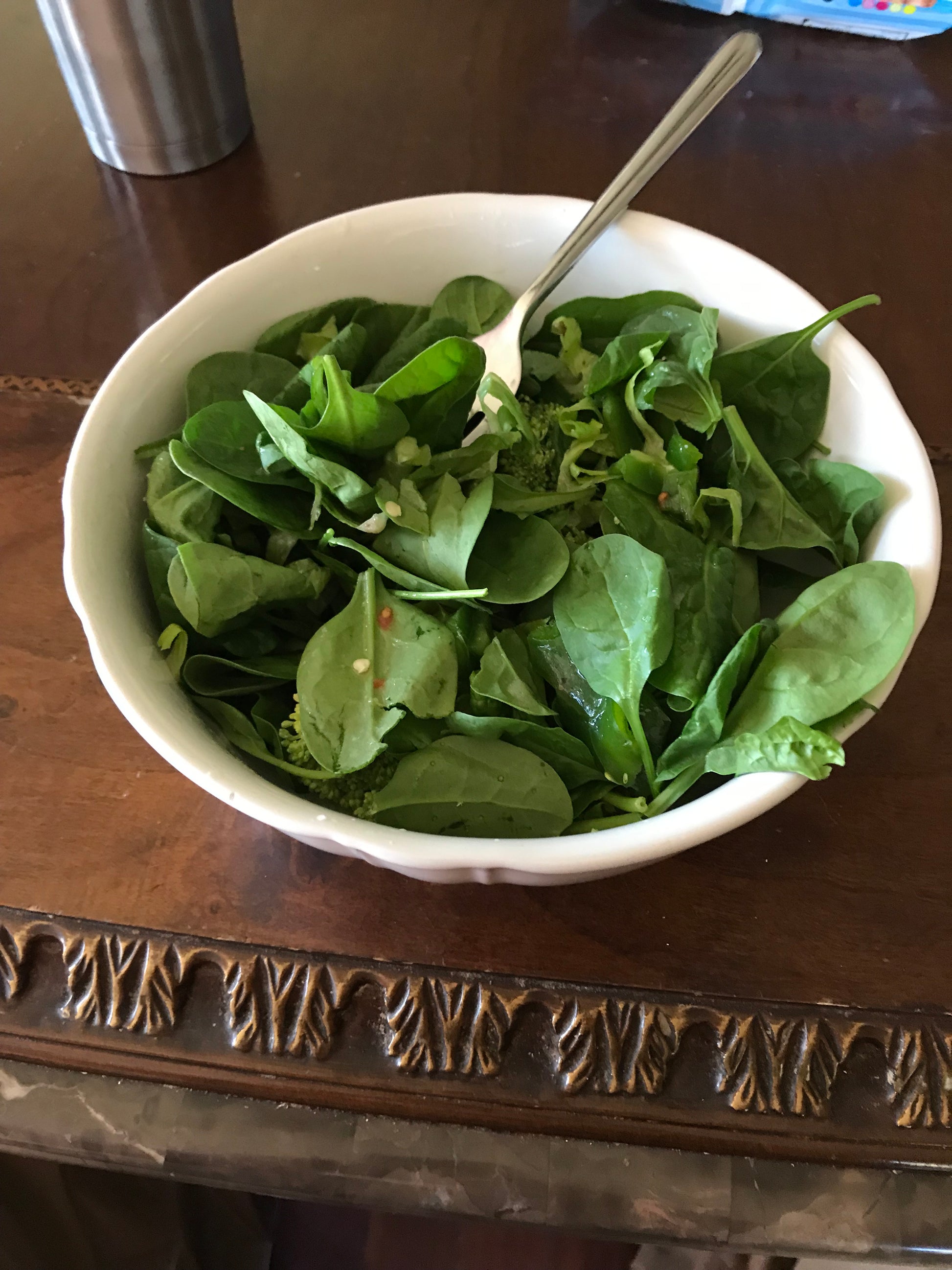 White bowl filled with fresh green spinach leaves on a wooden surface.