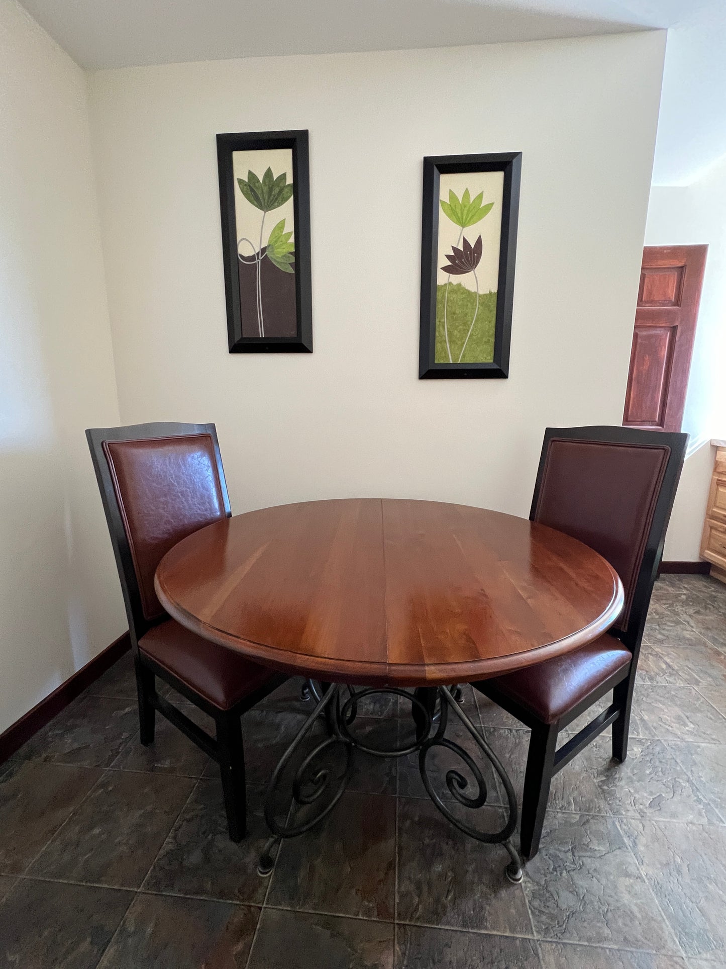 Round wooden table with four matching chairs in a room with framed pictures on the wall.