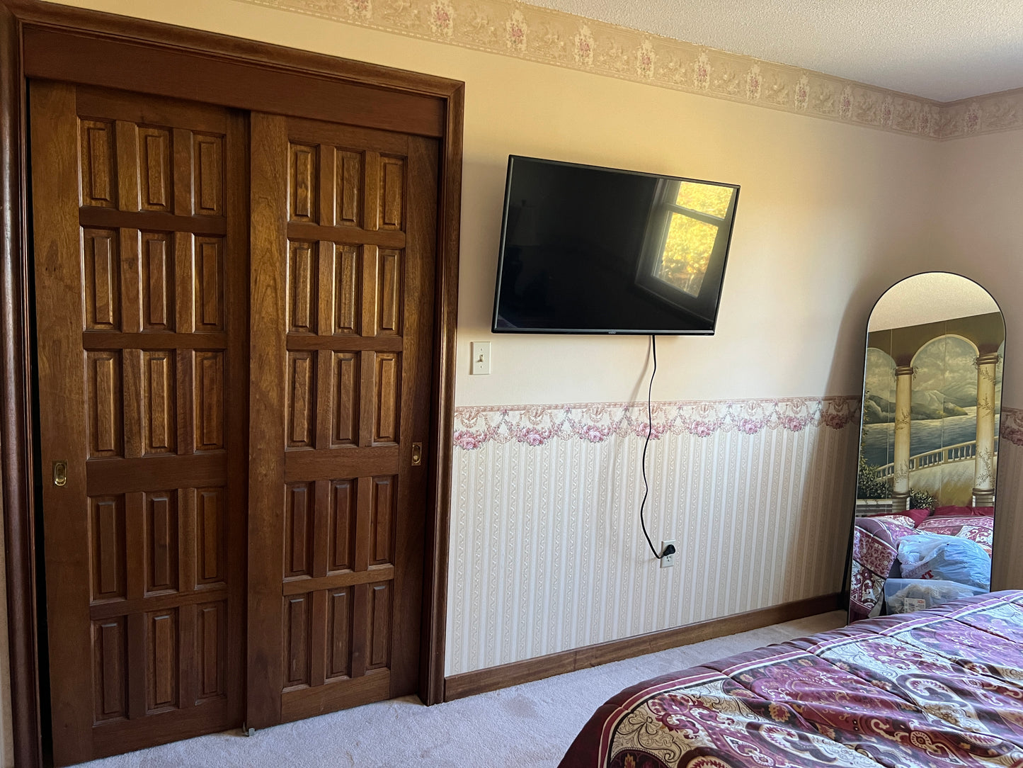 Bedroom with wooden door, TV on wall, and bed with patterned bedding.