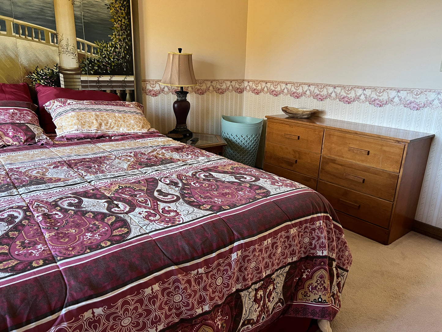Bedroom with a bed covered in a patterned comforter, wooden dresser, and lamp.