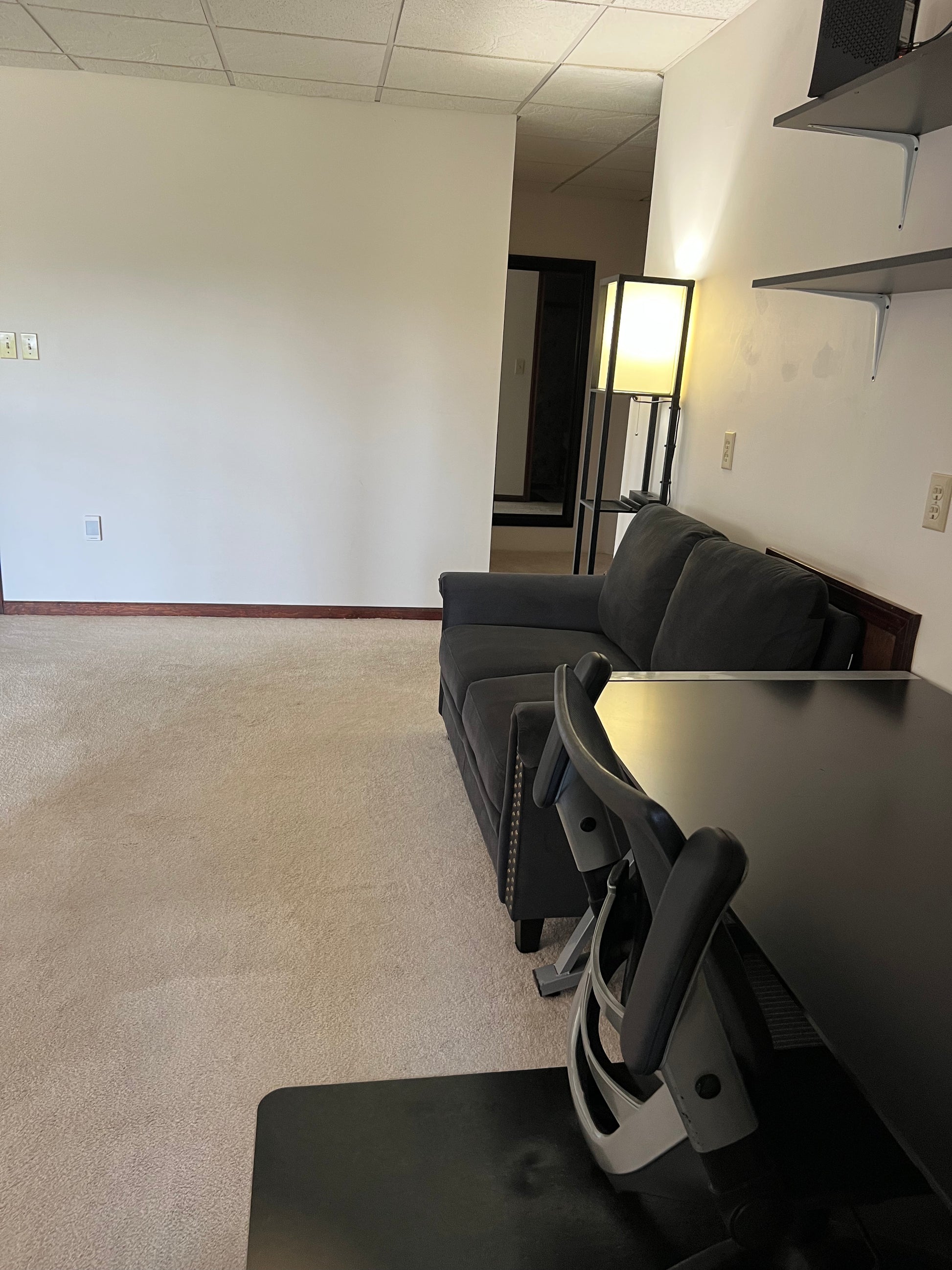 Modern office space with a gray sofa, black chairs, and a lamp.