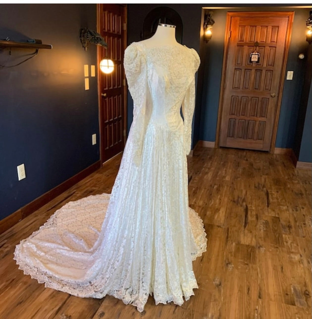 White lace wedding dress on a mannequin in a room with wooden floors and doors.