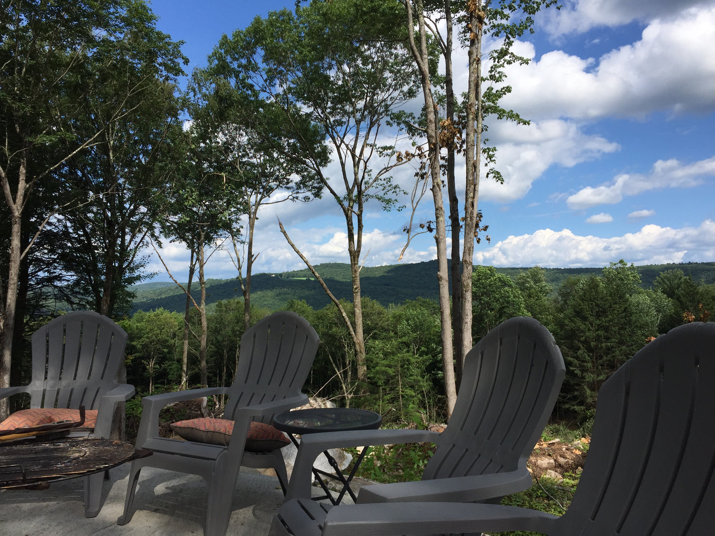 Outdoor patio with Adirondack chairs and a scenic view of trees and mountains.