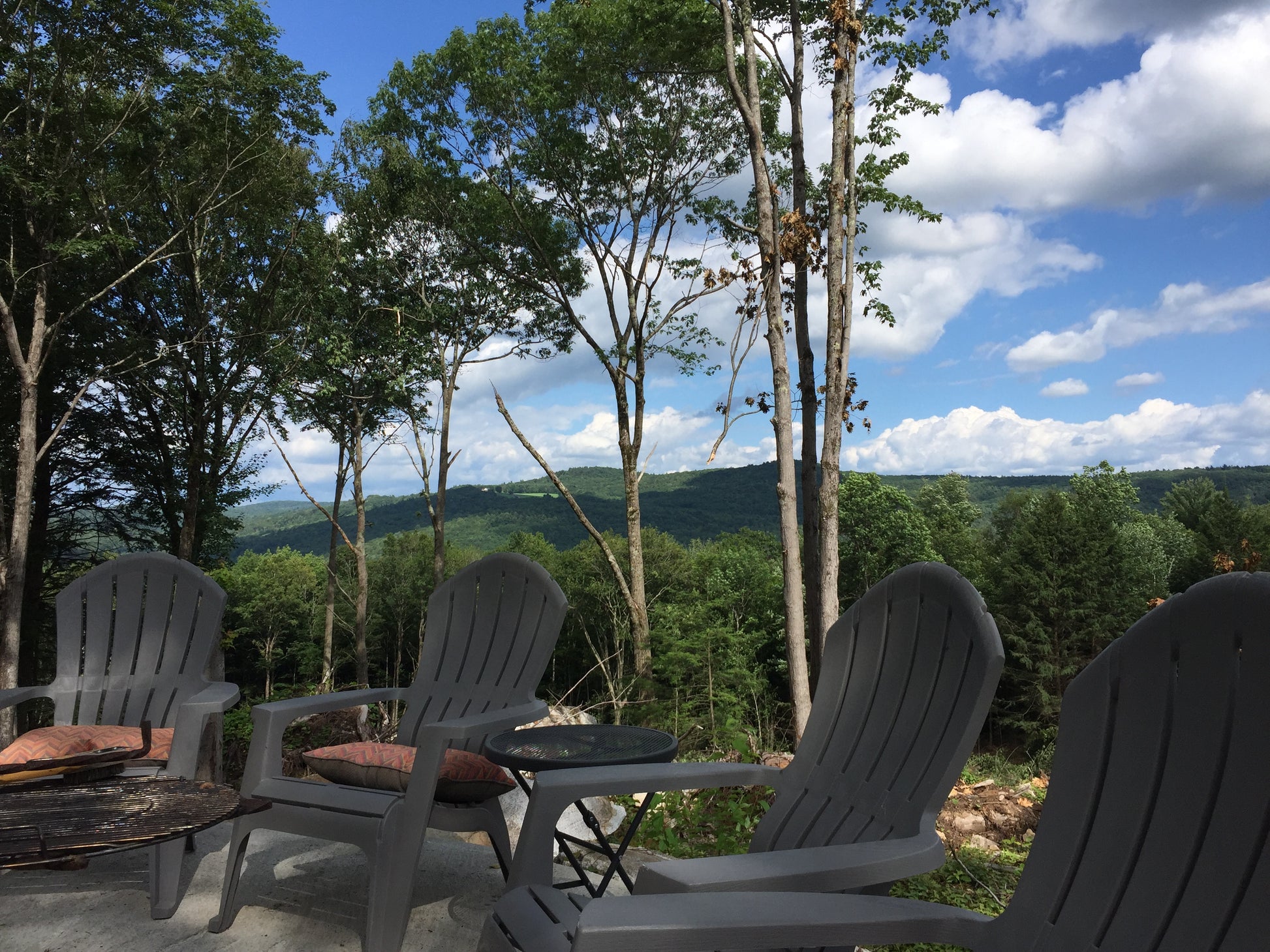 Outdoor patio with Adirondack chairs and a scenic view of trees and mountains.