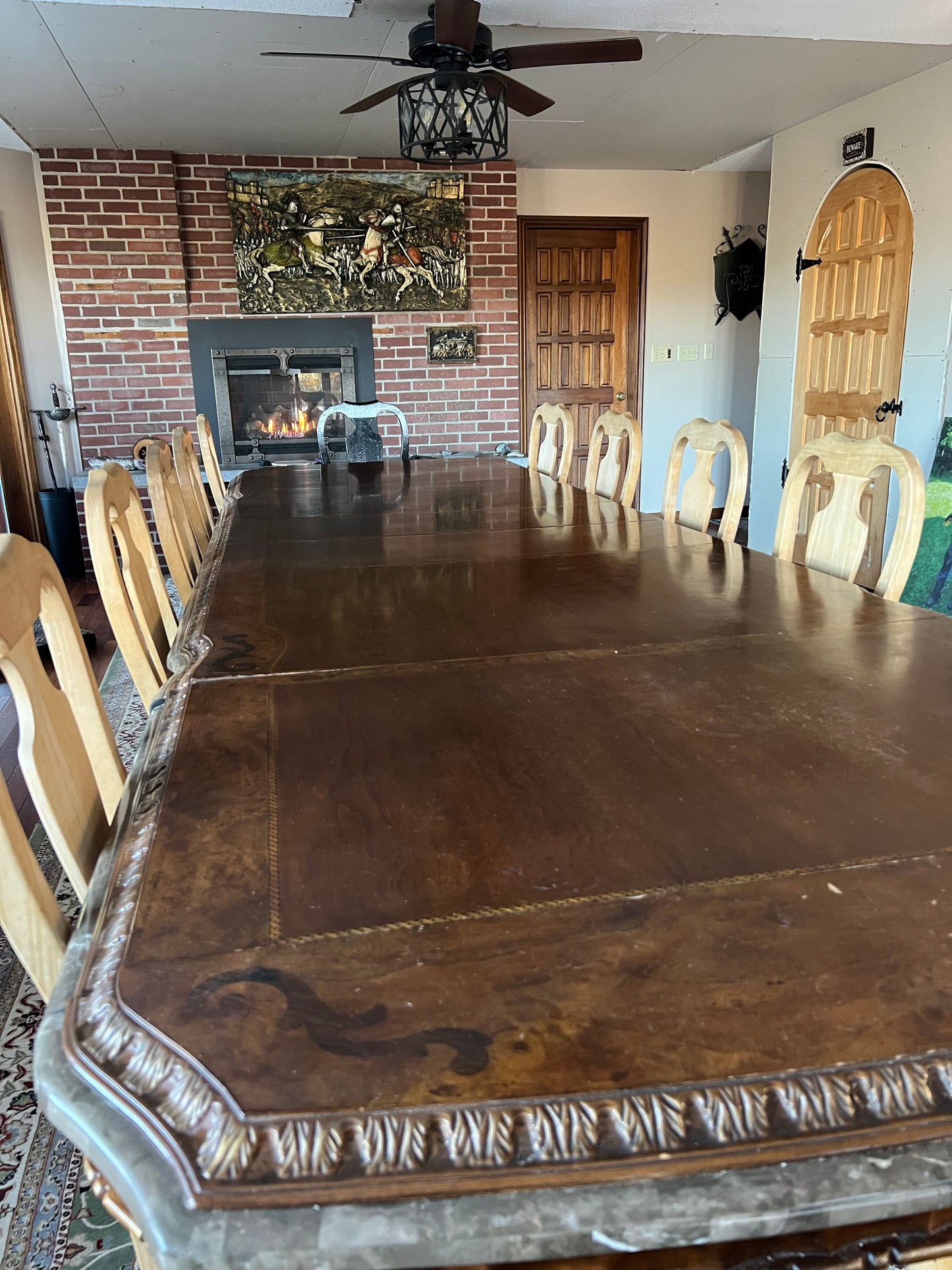 Large ornate fireplace  with a wooden arched frame door to closet. With a room and chairs visible.